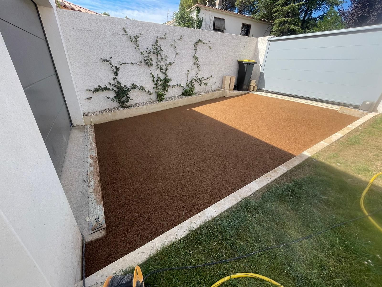 Chemin extérieur en gravier rouge bordé de pelouse verte et de murs blancs.