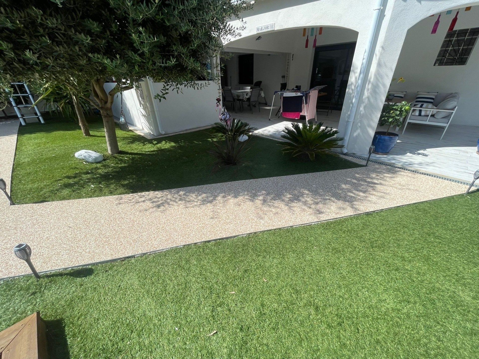 Allée en gravier beige menant à une maison avec une pelouse verte et des arbres.