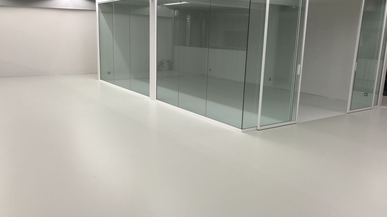Sol en résine grise dans un espace intérieur avec des cloisons vitrées.
