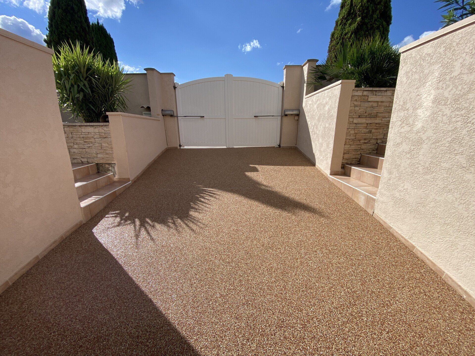 Allée en gravier rouge bordé de murs en béton et de végétation.