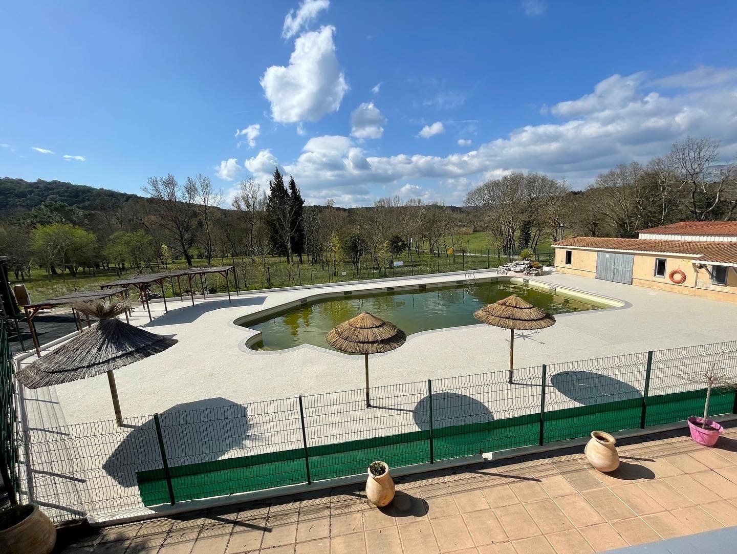 Piscine rectangulaire entourée de gravier beige avec des chaises longues et une vue sur les collines.