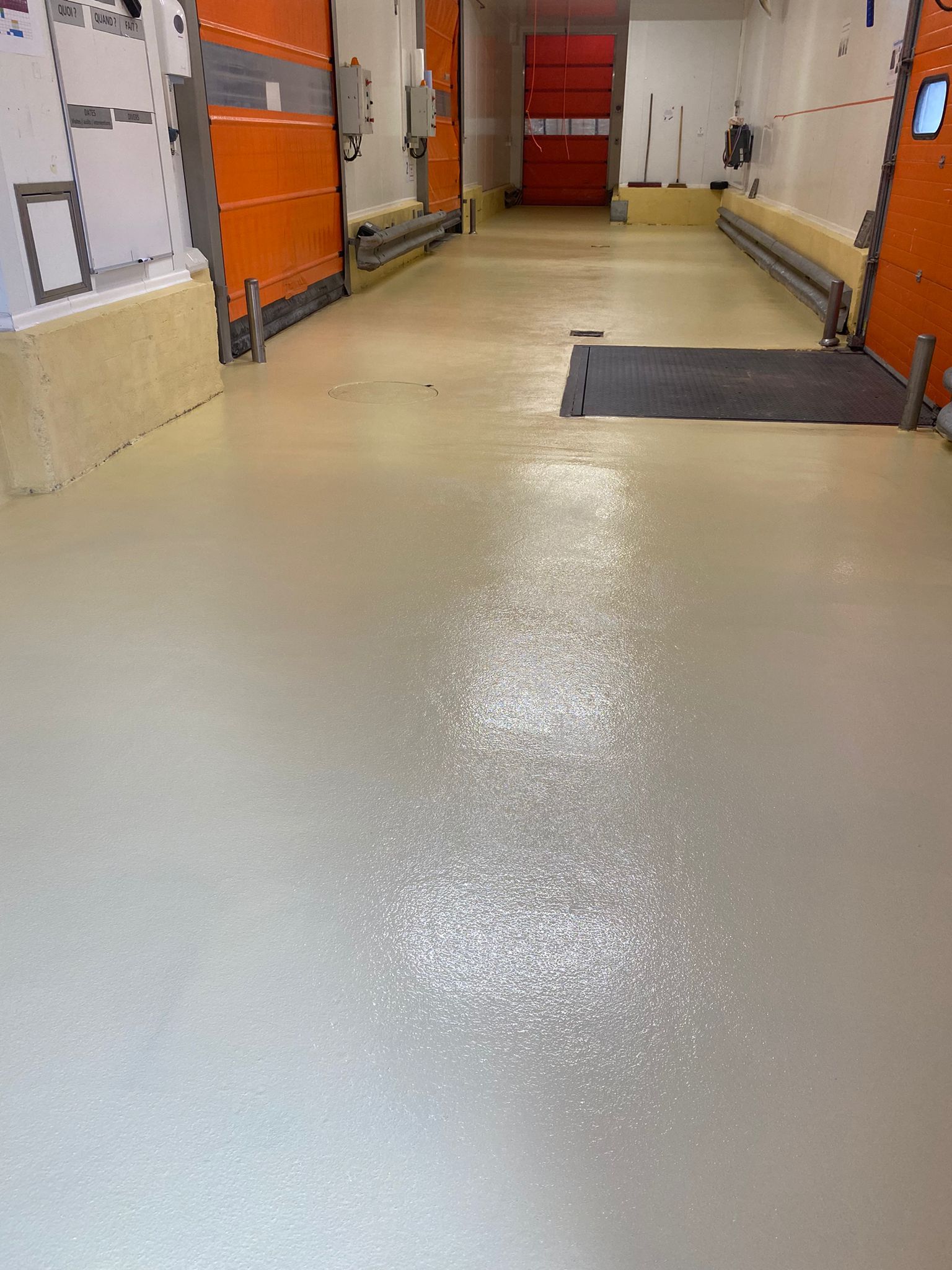 Sol lisse et brillant en résine ou béton ciré, de couleur claire.