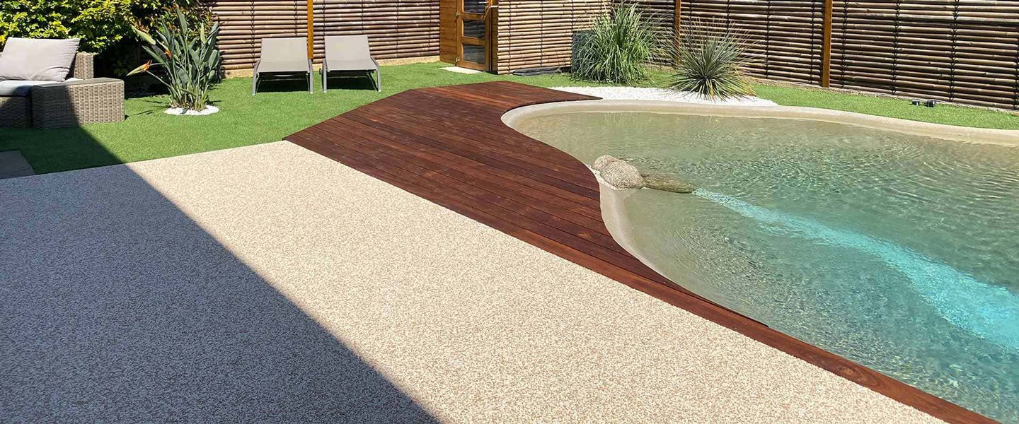 Allée en gravier beige et rouge menant à une piscine avec une pelouse verte et une maison en arrière-plan.