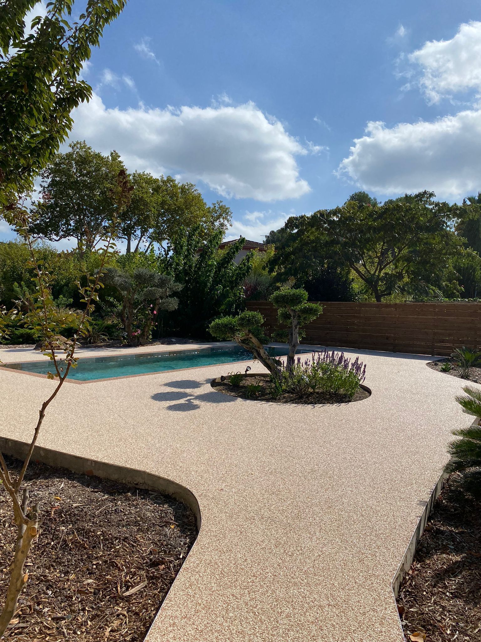 Aménagement paysager autour d'une piscine avec sol en résine et massifs arborés.