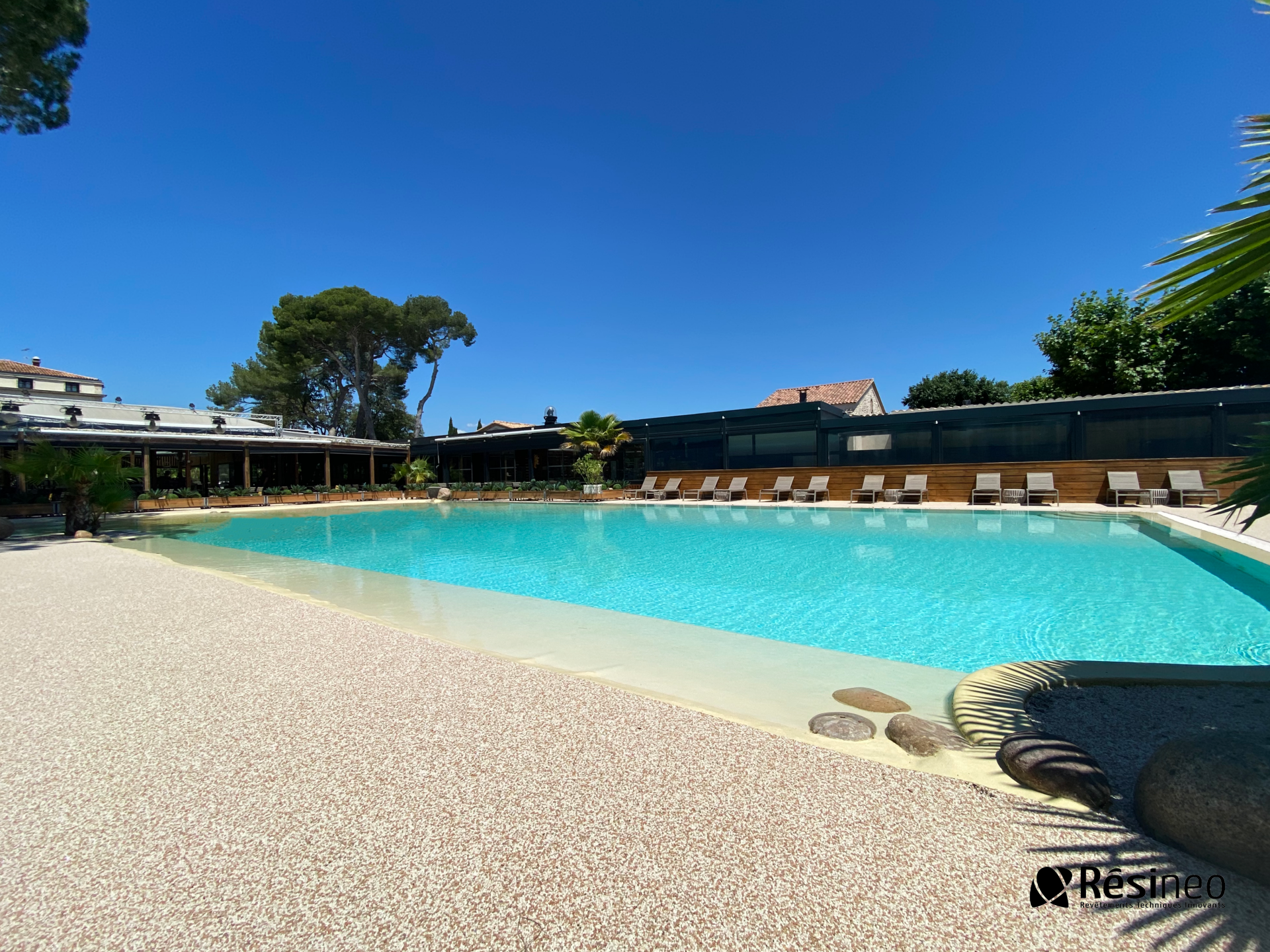 Grande piscine entourée de gravier blanc avec des transats et une vue sur l'océan.