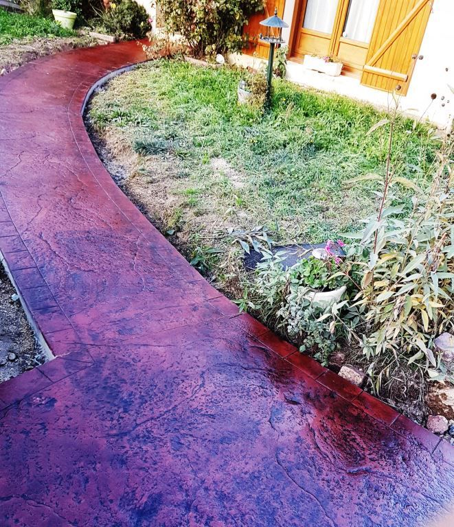 Béton imprimé pourpre dans chemin traversant un petit jardin direction l'entrée d'une maison.