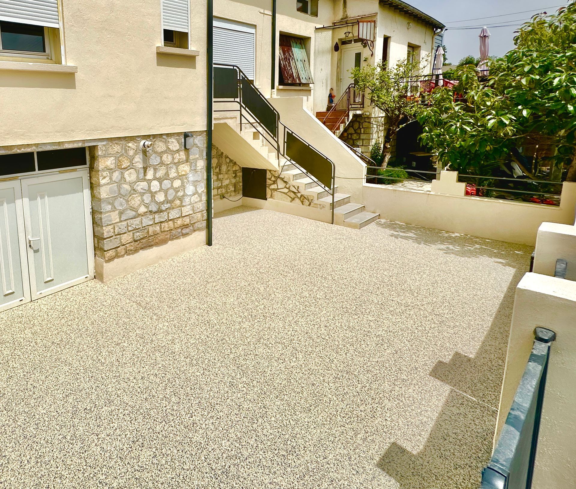 Allée en gravier fin menant à une maison, avec des escaliers et des murs en pierre.