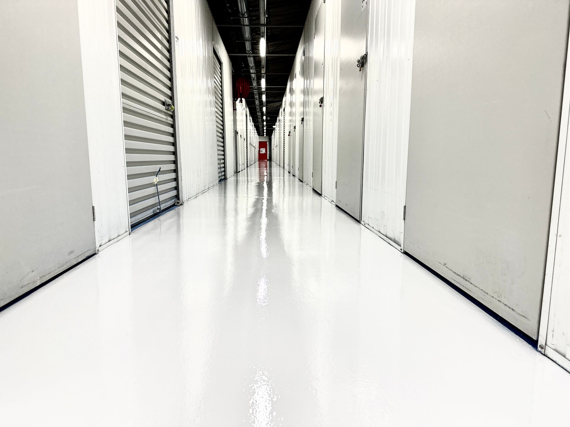 Allée intérieure en résine blanche brillante, bordée de murs blancs et de portes de garage.