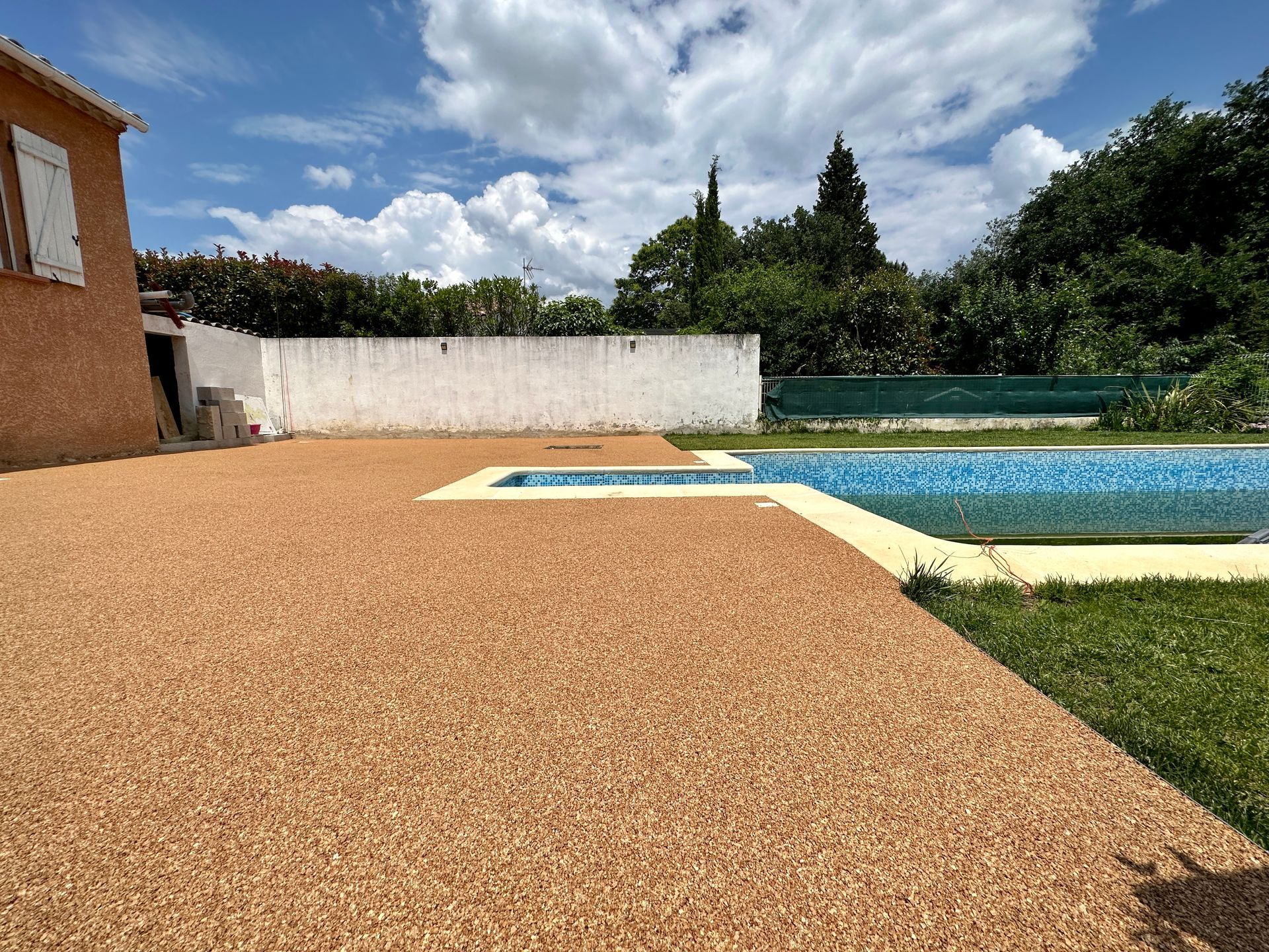 Piscine rectangulaire entourée de gravier fin et de pelouse, avec des arbres en arrière-plan.