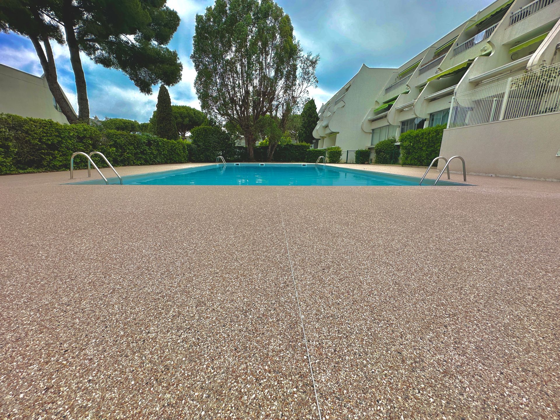 Piscine entourée de gravier fin et de palmiers, avec une vue sur un jardin paysager.