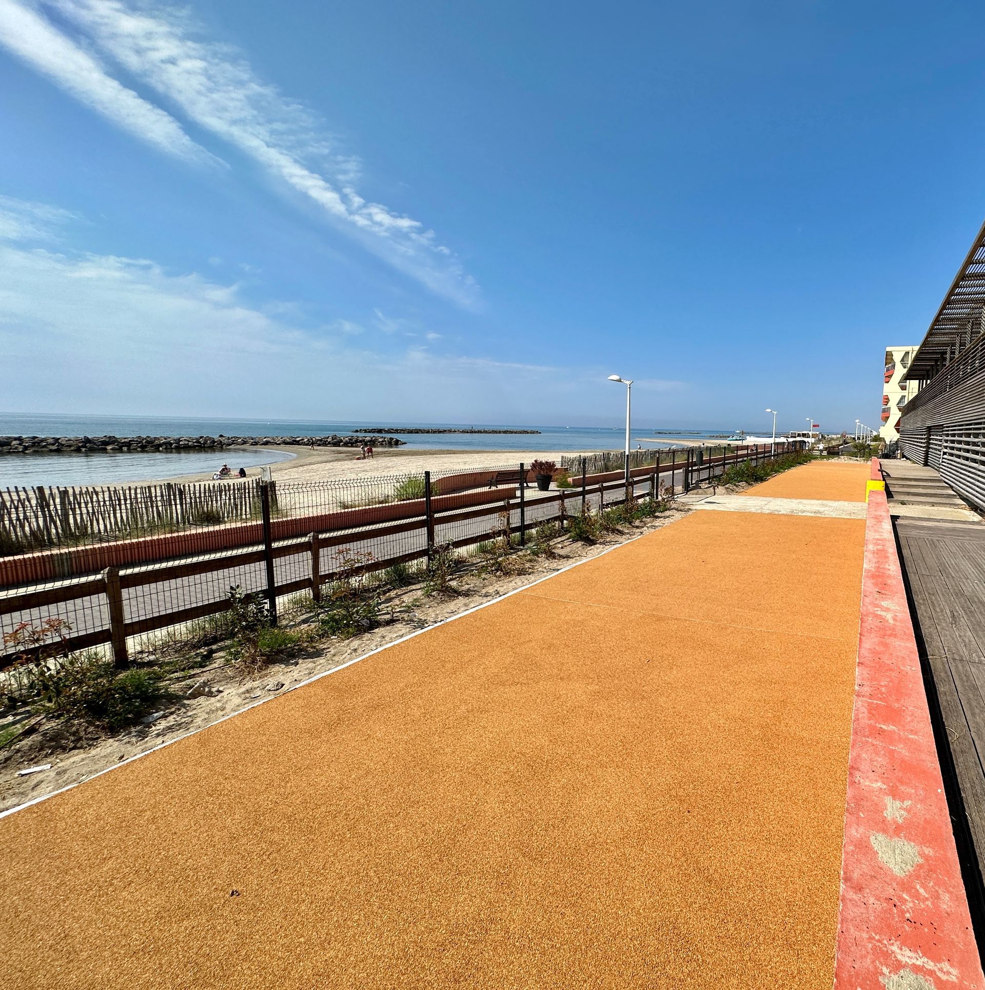 Allée en gravier rouge bordée de clôtures en bois, menant vers un paysage ouvert.