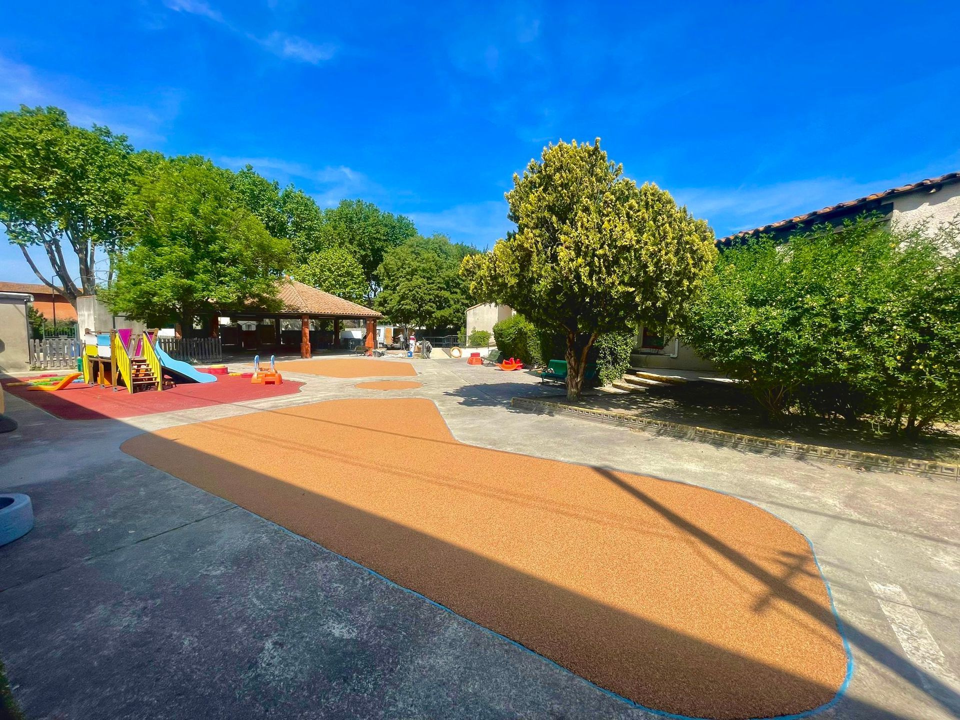 Allée en gravier rouge dans un parc, avec des arbres et des bancs en arrière-plan.