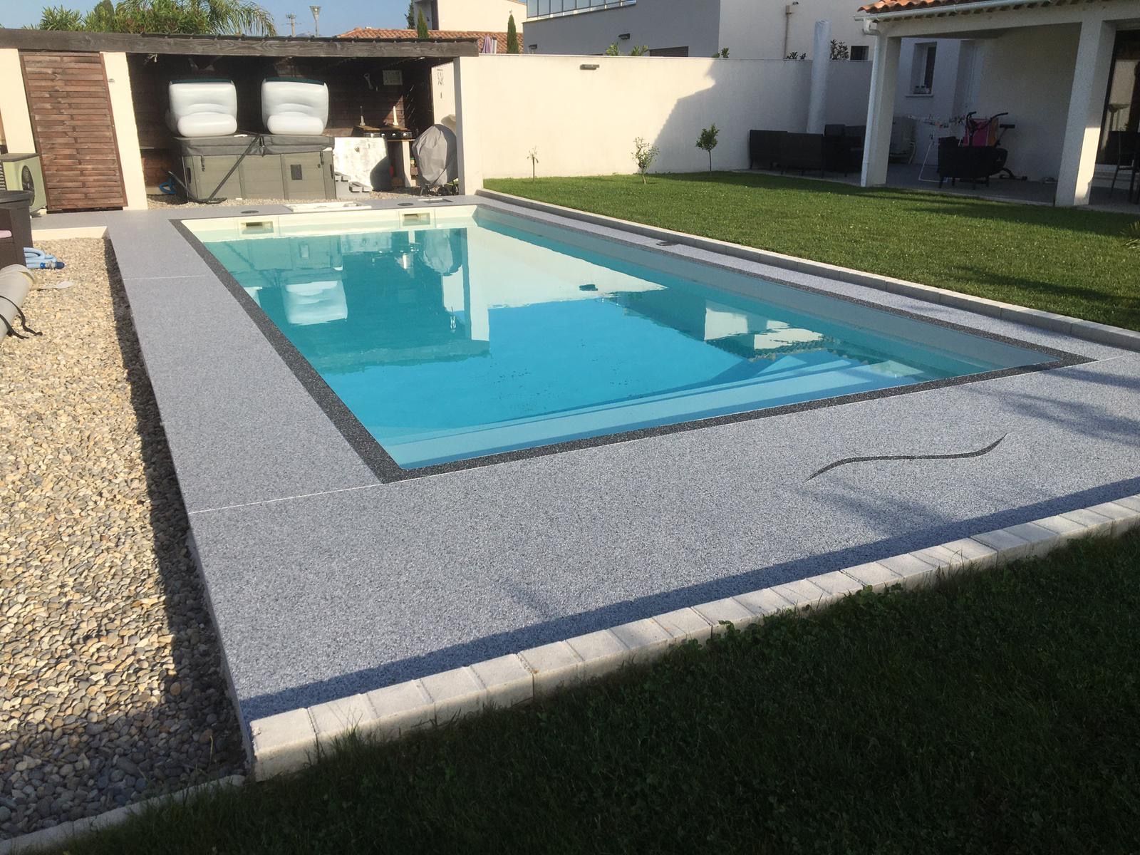 Piscine rectangulaire entourée de gravier blanc et de pelouse verte.