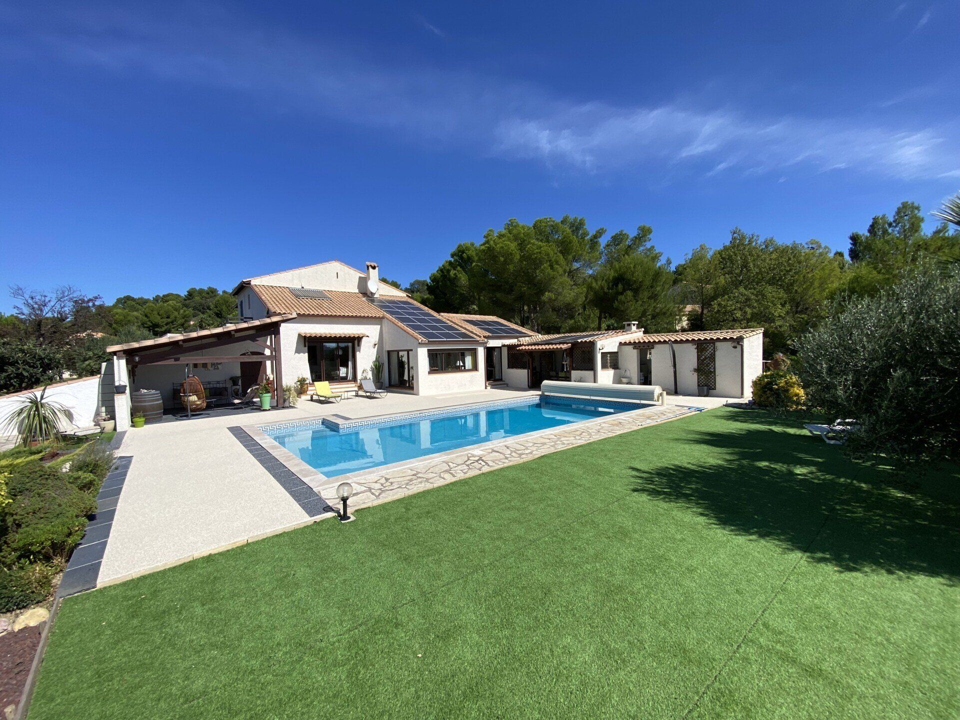Résine drainante coulée autour d'une piscine creusée dans propriété moderne avec herbe synthétique et panneaux photovoltaïques sur le toit.