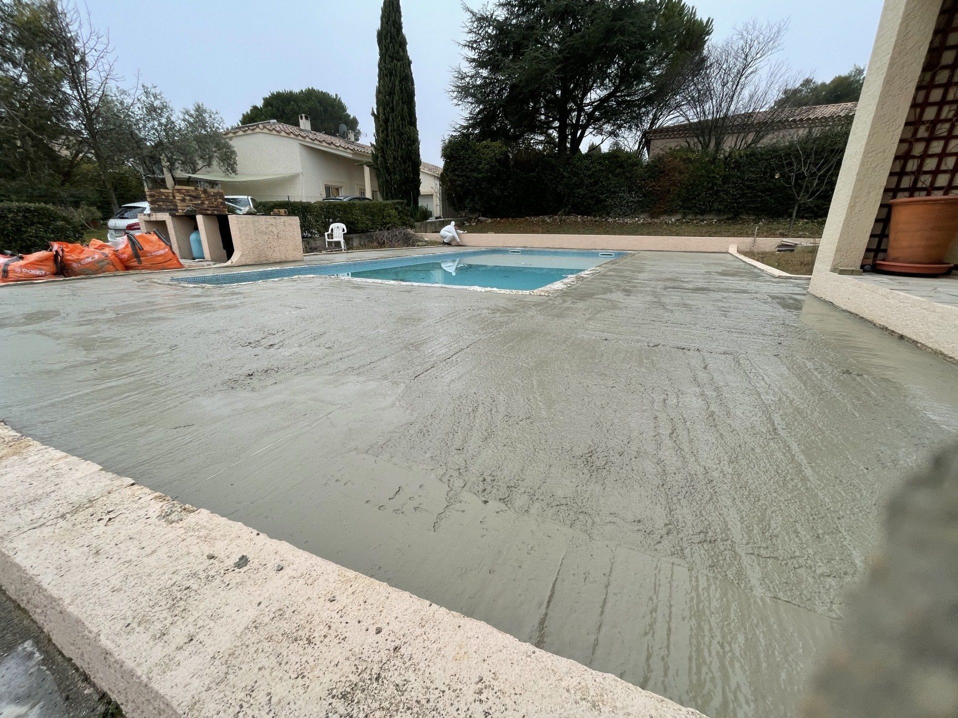 Terrasse en construction autour d'une piscine avec une surface en béton brut et des équipements de chantier.