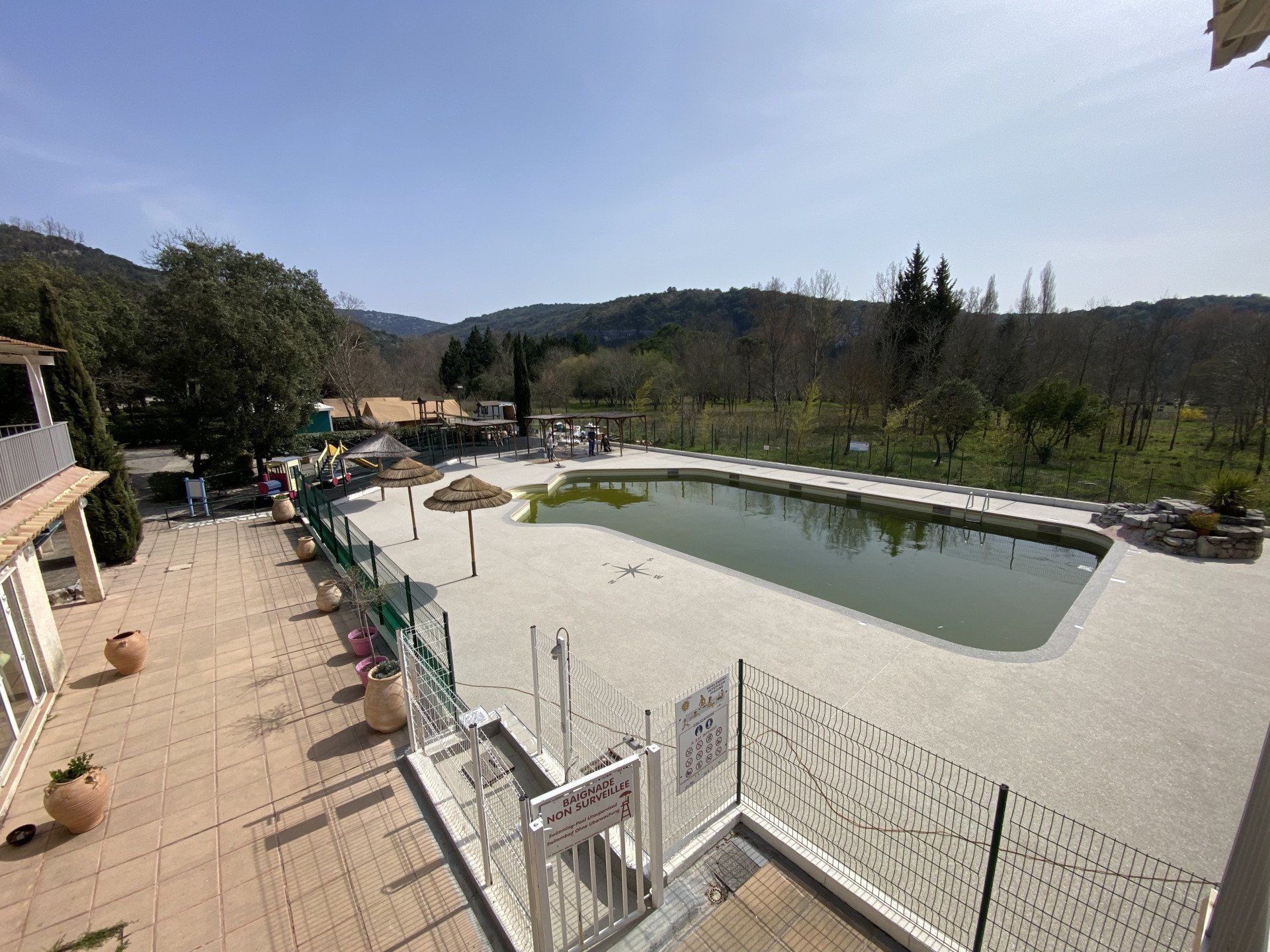 Piscine rectangulaire entourée de gravier beige avec des chaises longues et une vue sur les collines.