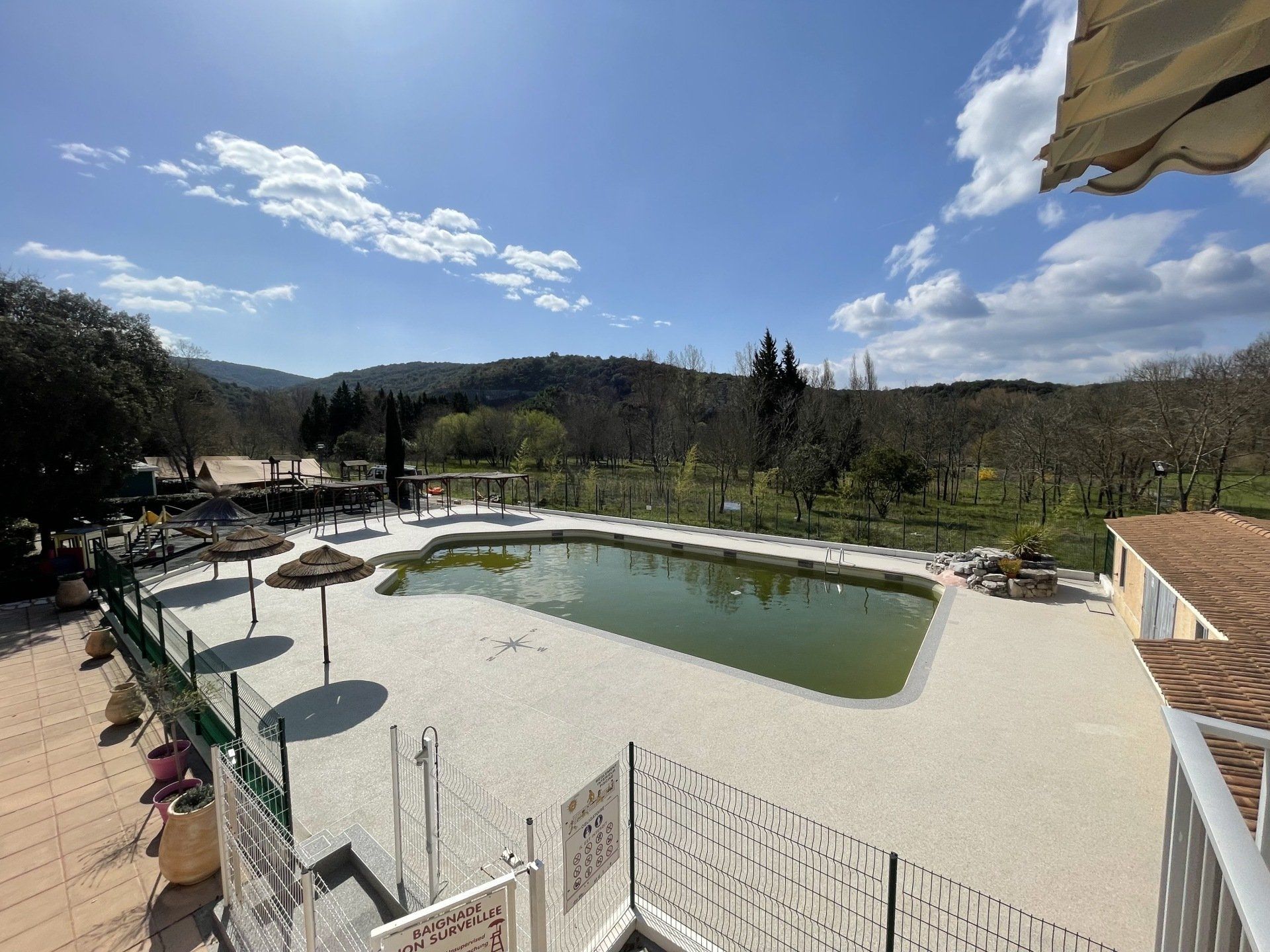 Piscine rectangulaire entourée de gravier beige avec des chaises longues et une vue sur les collines.