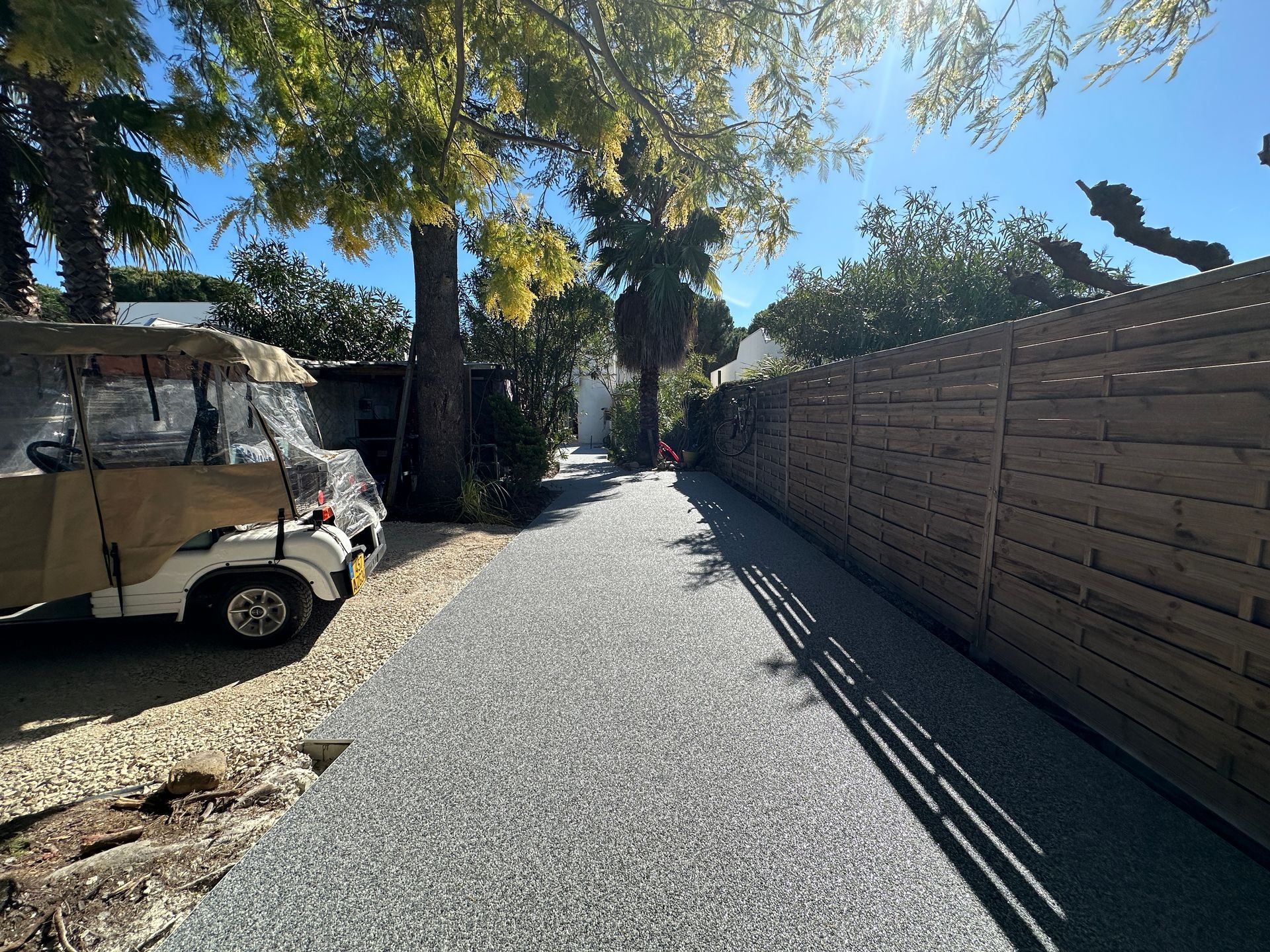 Allée en gravier blanc bordée d'un mur en briques et d'arbres.