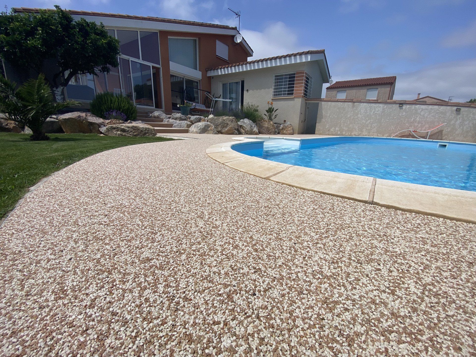 Piscine entourée de gravier beige avec une maison en arrière-plan.