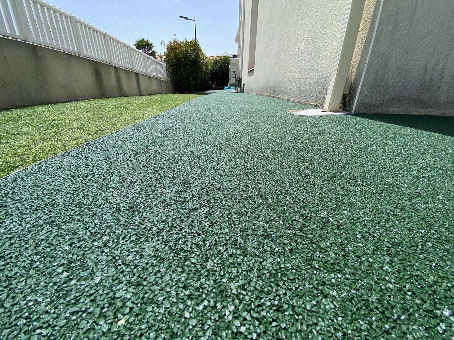 Surface en gravier vert entourée de murs en béton et de végétation.