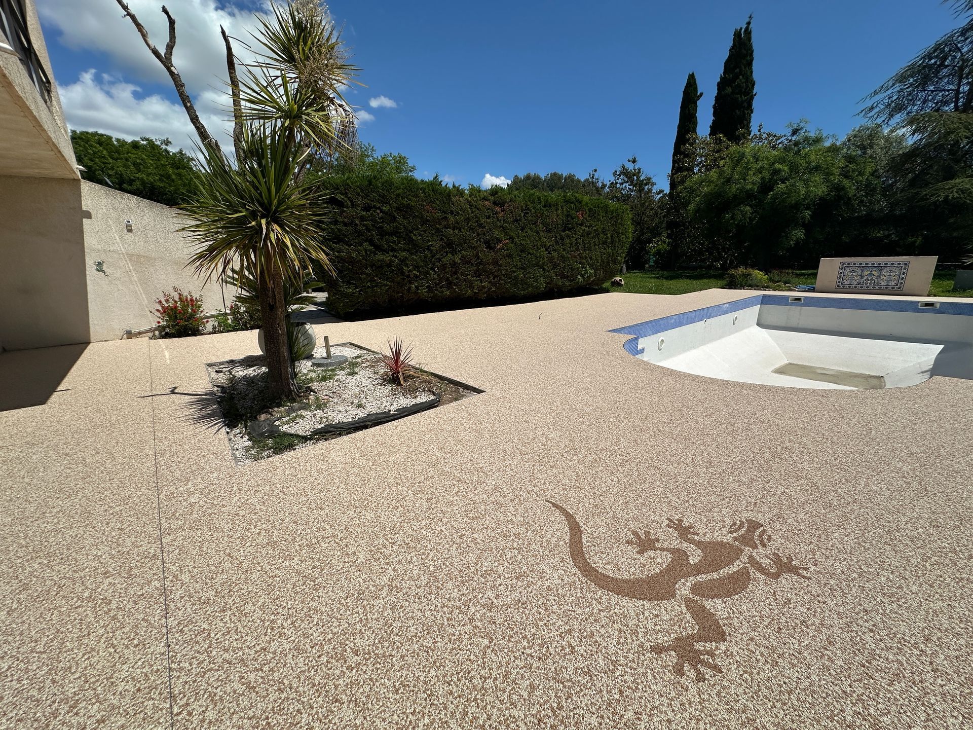 Grande cour avec sol en résine décorative, palmiers et motif de style tribal.