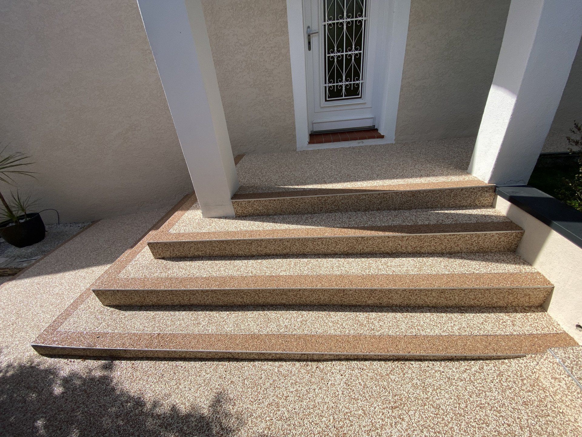 Escalier en gravier beige menant à une maison avec des murs blancs et des fenêtres.