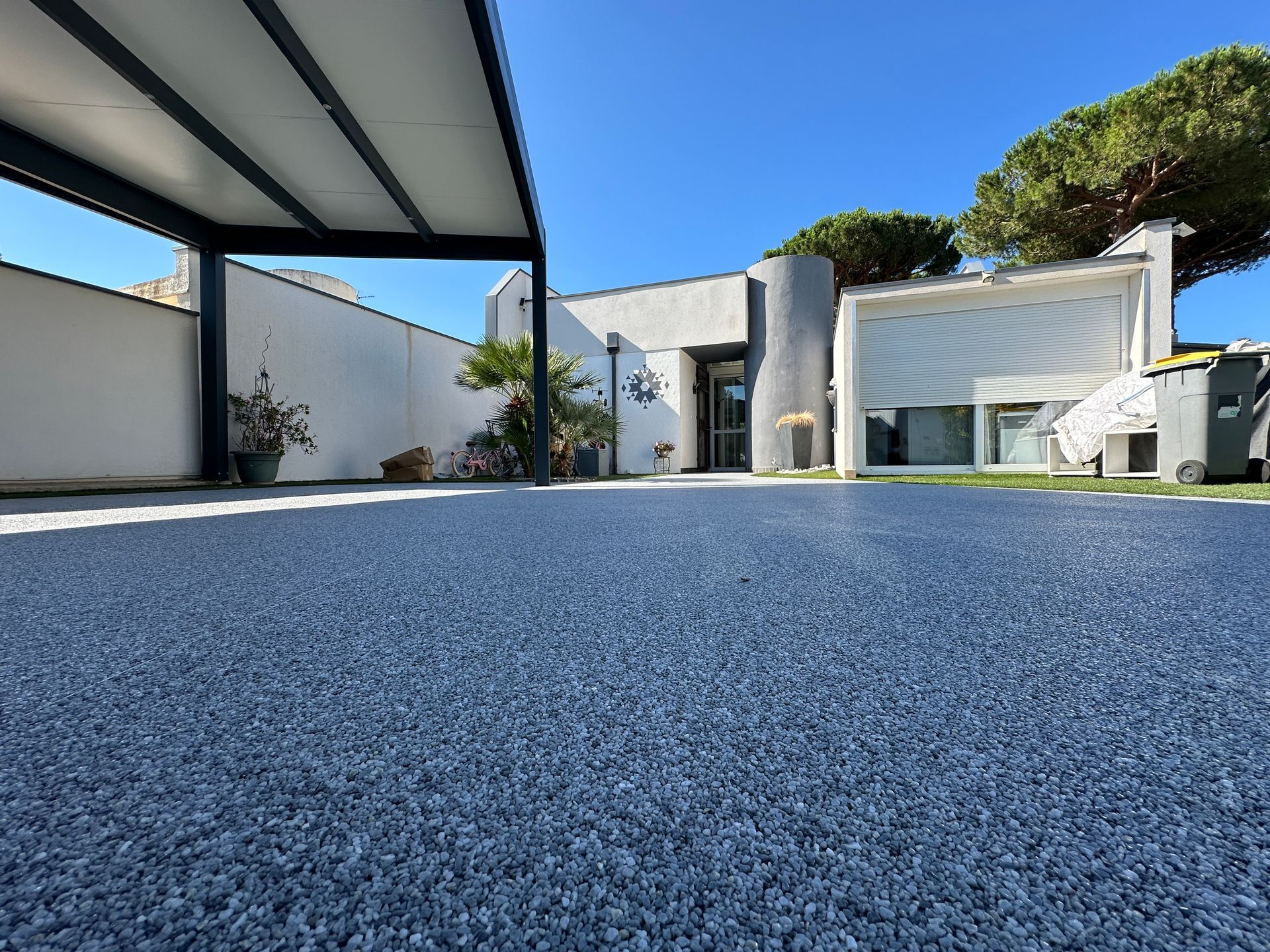 Allée en résine gravillonnée bleue, couverte et bordée de végétation.