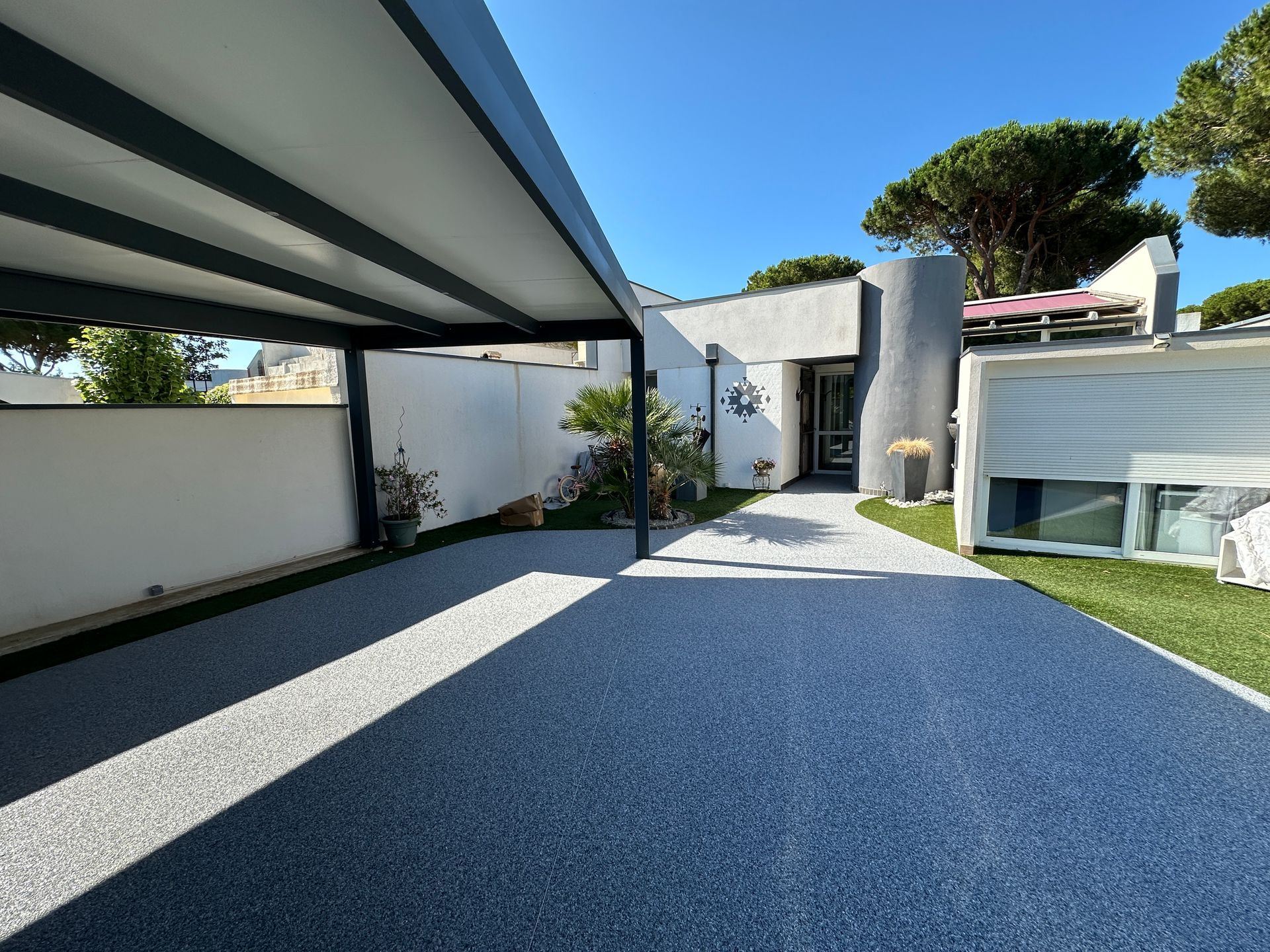Allée d'entrée couverte avec sol en résine gravillonnée menant à une maison moderne.