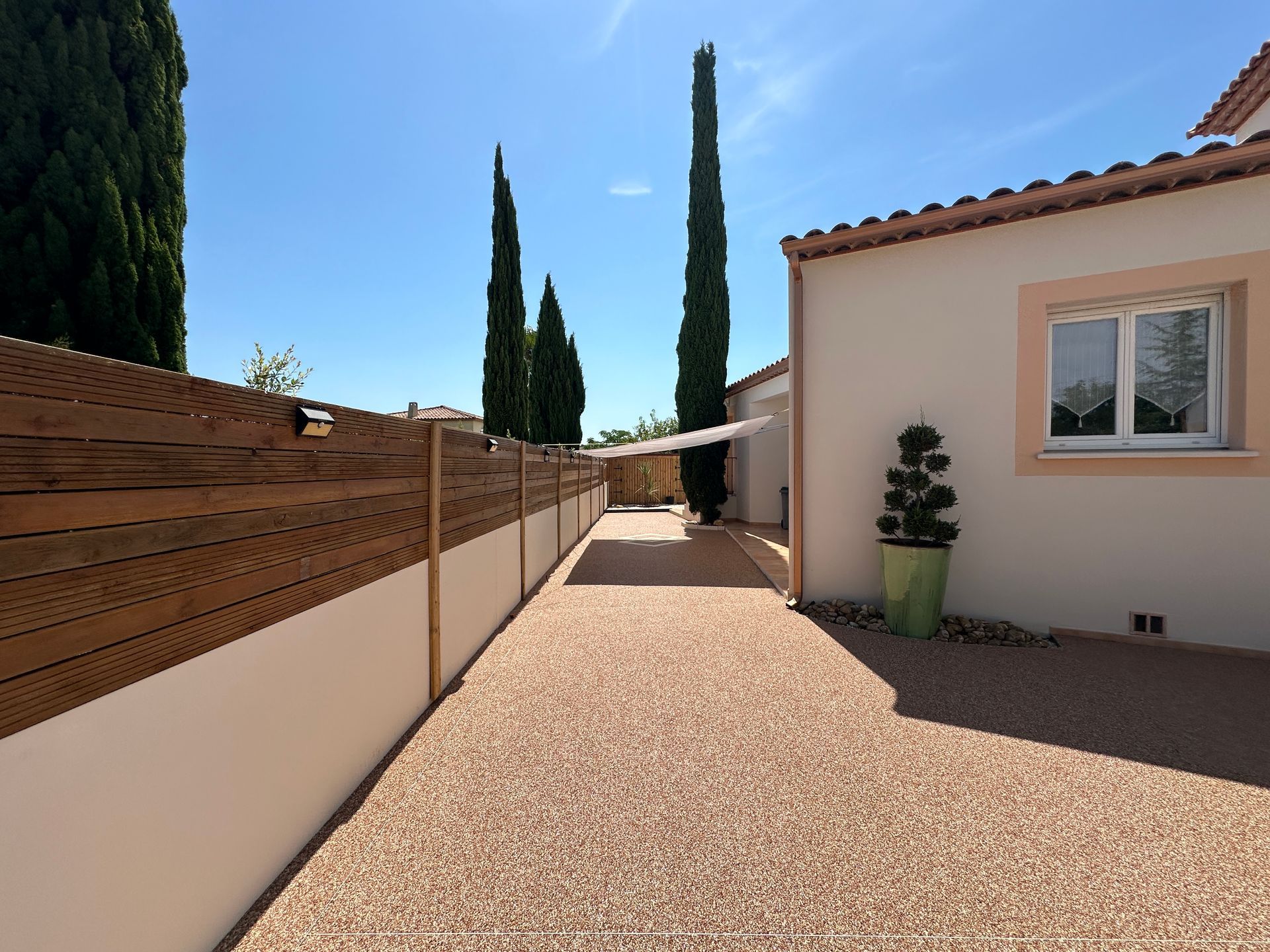 Chemin en résine gravillonnée menant à une maison, bordé d'une clôture en bois.
