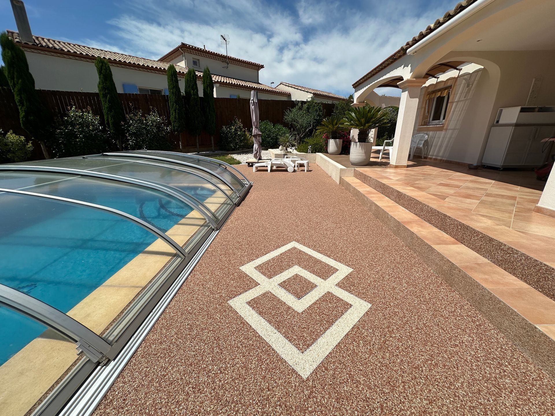 Accès à une maison avec plage de piscine en résine et motif géométrique blanc.