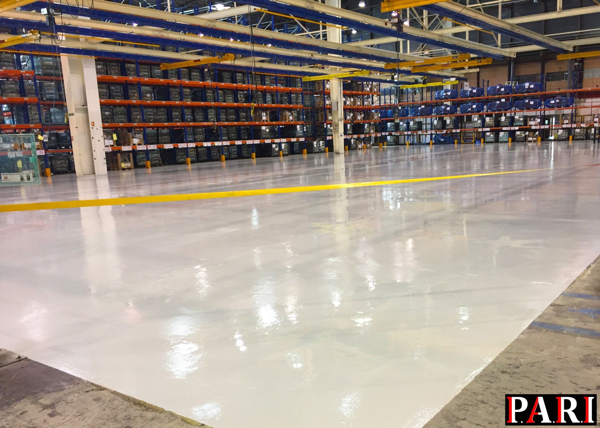 Sol en résine brillante dans un entrepôt avec des étagères métalliques en arrière-plan.