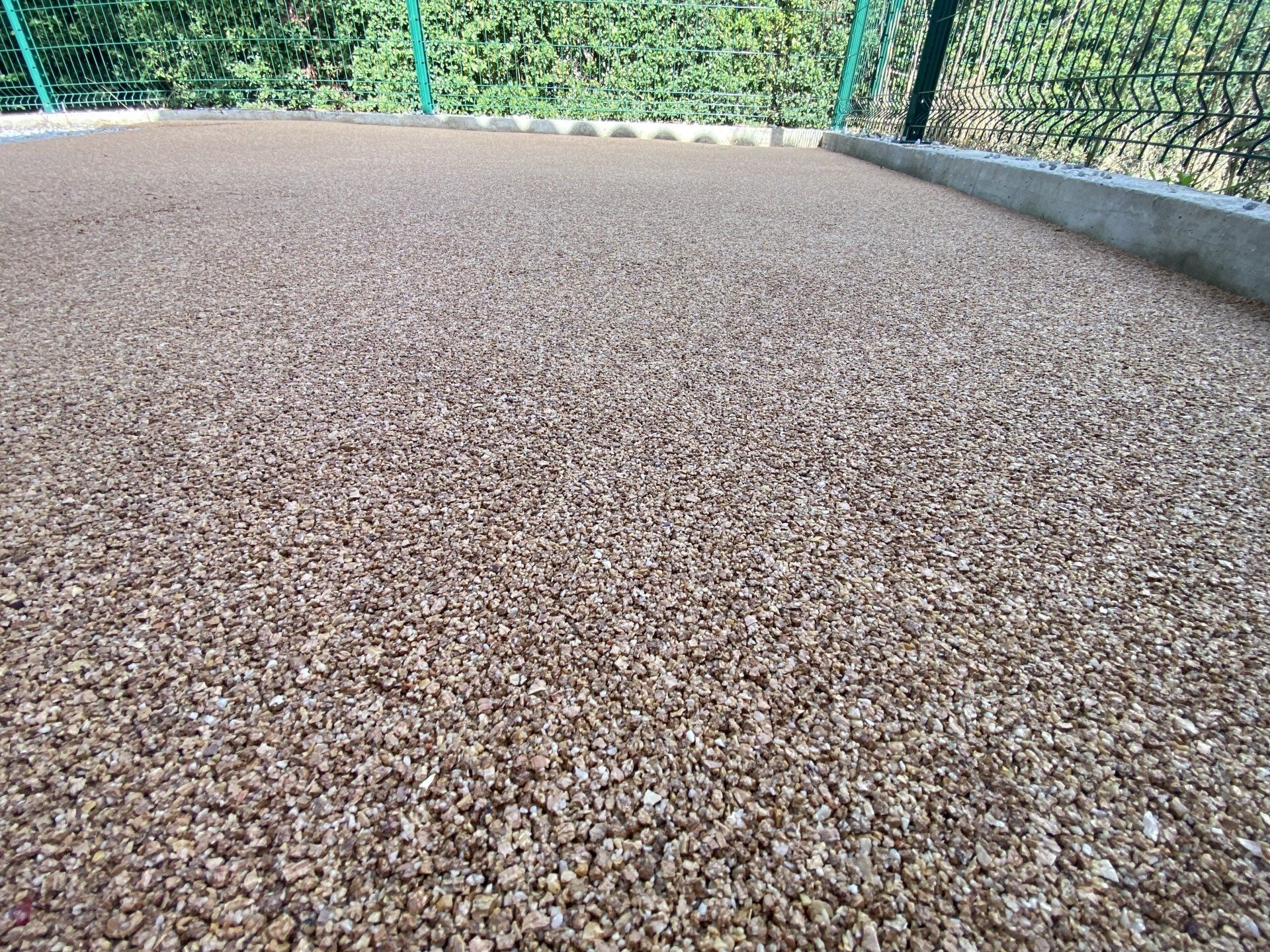 Allée en gravier gris avec une bordure en béton et une vue sur un jardin.
