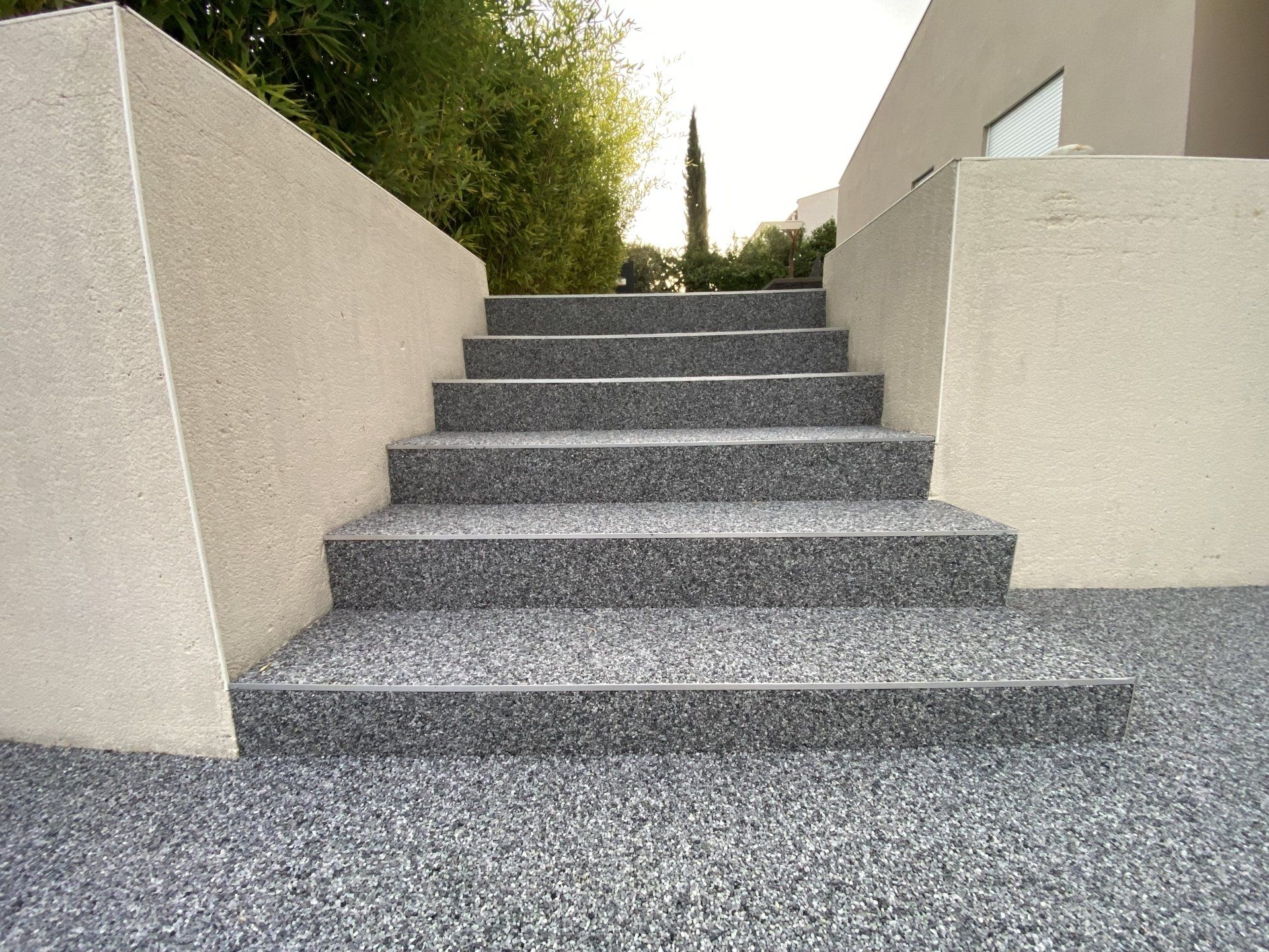 Escalier en gravier gris avec des marches blanches et des murs beiges.