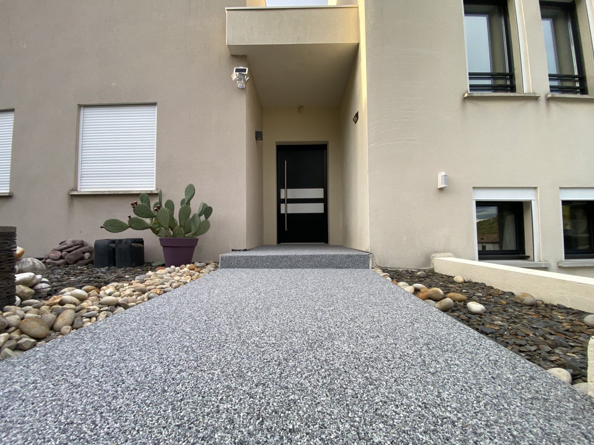 Allée en gravier gris menant à un batiment avec porte et fenêtres.