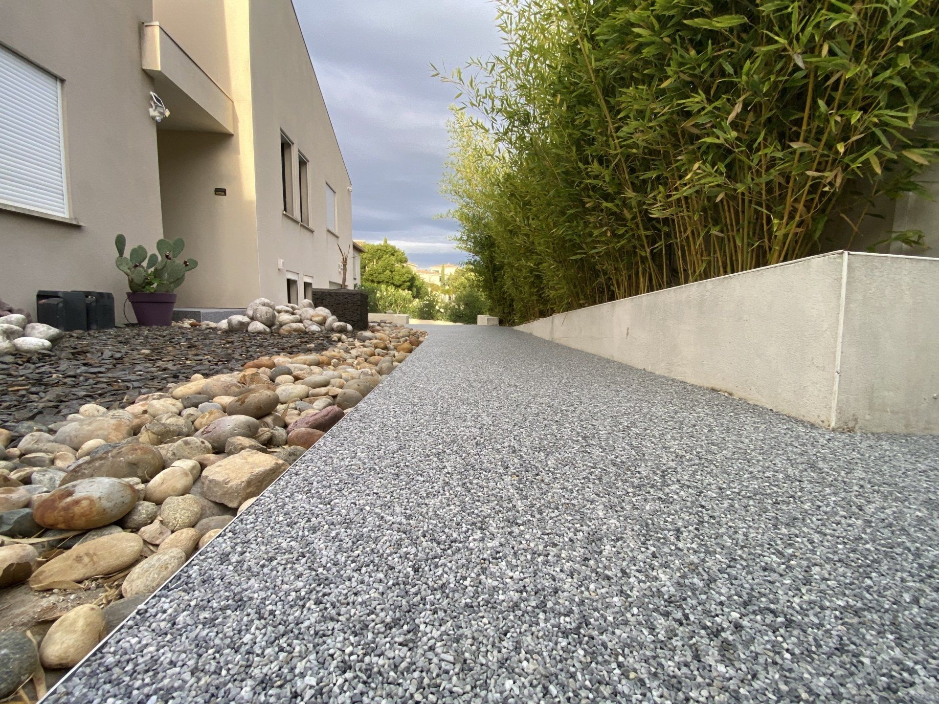Allée en gravier gris avec des bordures en pierres naturelles et des bambous.