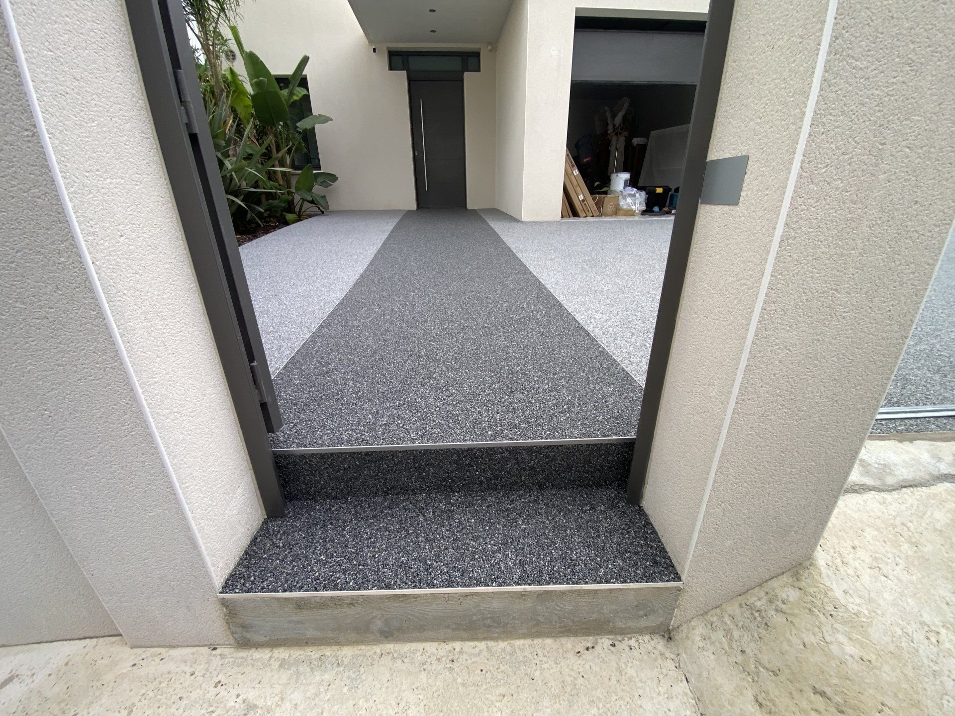 Allée en gravier gris bordée de murs blancs menant à une entrée.