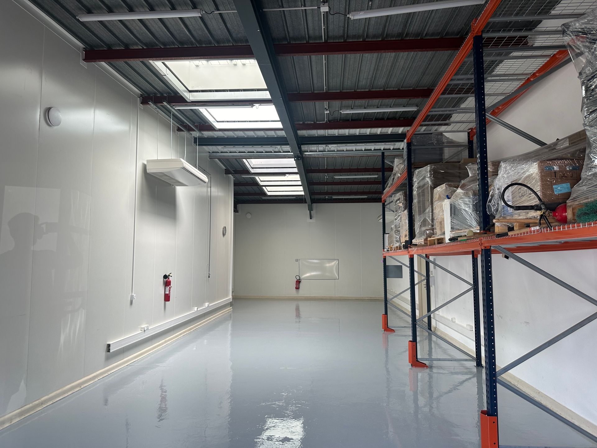 Entrepôt industriel avec sol en résine brillant, rayonnages métalliques et éclairage zénithal.