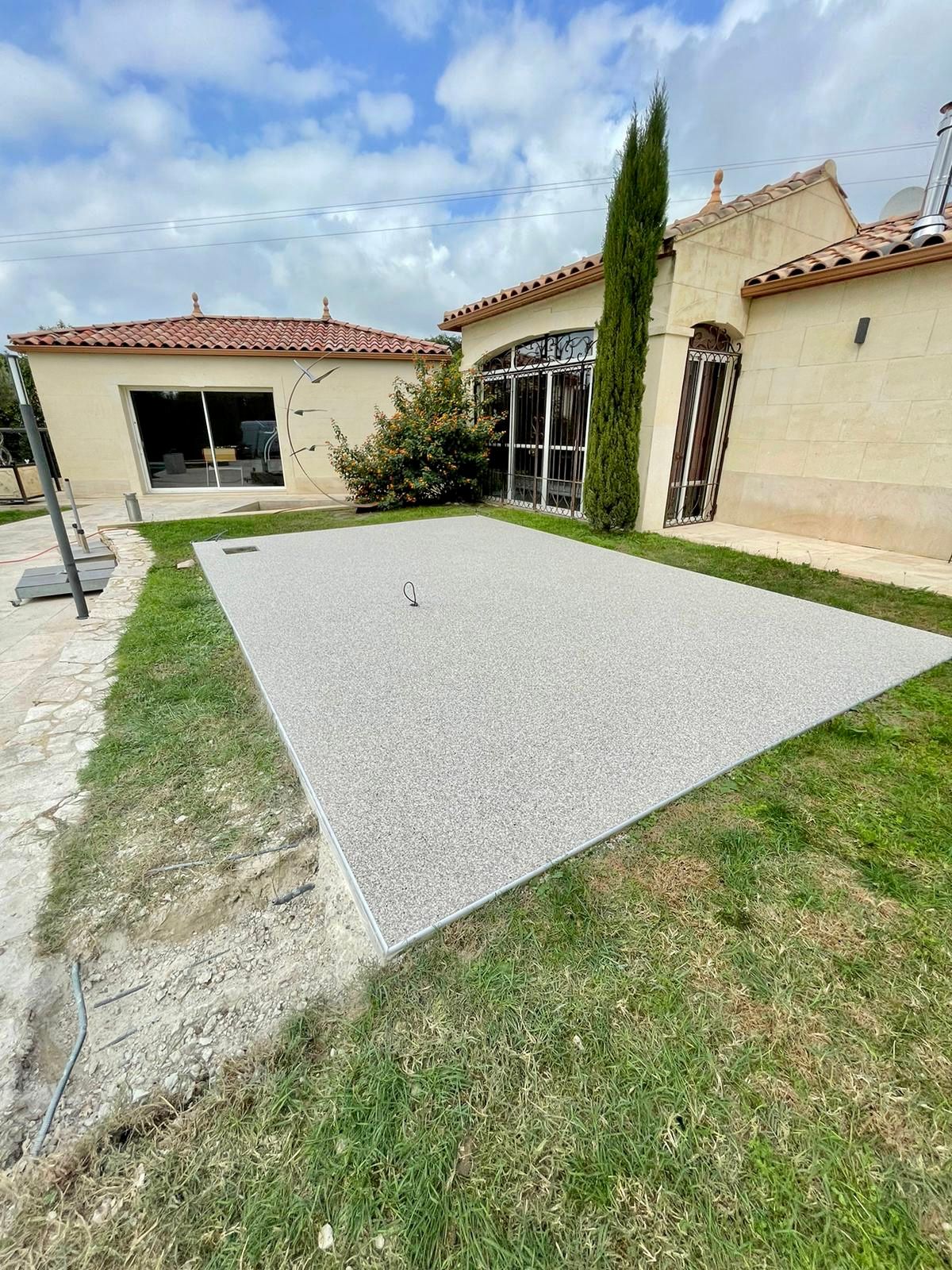 Terrasse en gravier blanc avec des bordures en pelouse verte et une maison en arrière-plan.