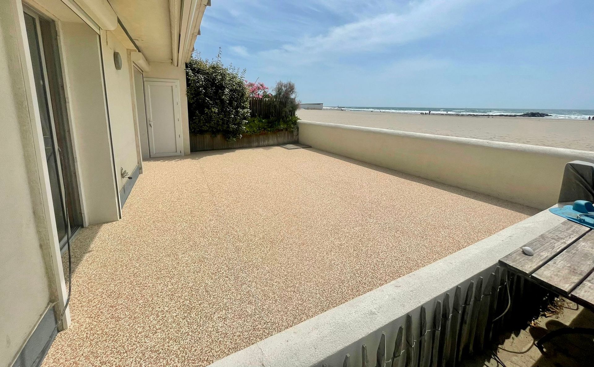 Terrasse en gravier avec vue sur l'océan et une clôture en béton.