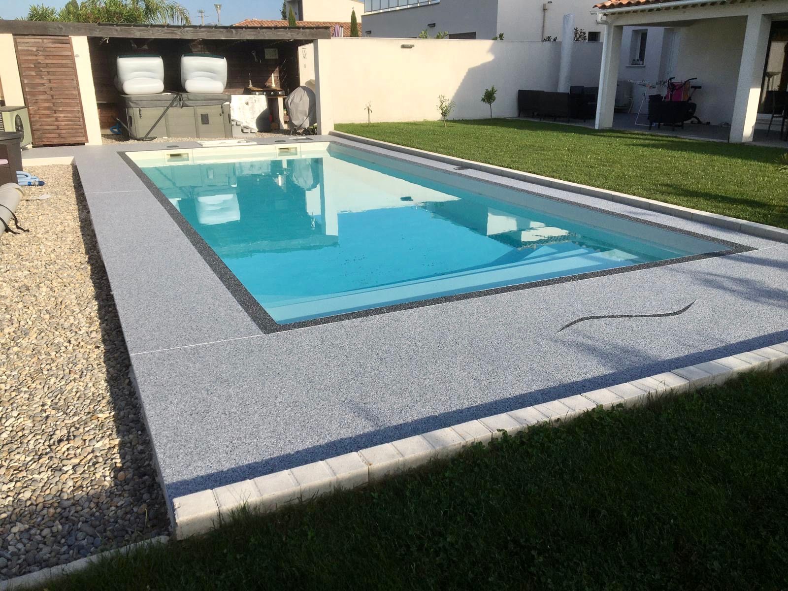 Piscine rectangulaire entourée de gravier blanc et de pelouse verte.