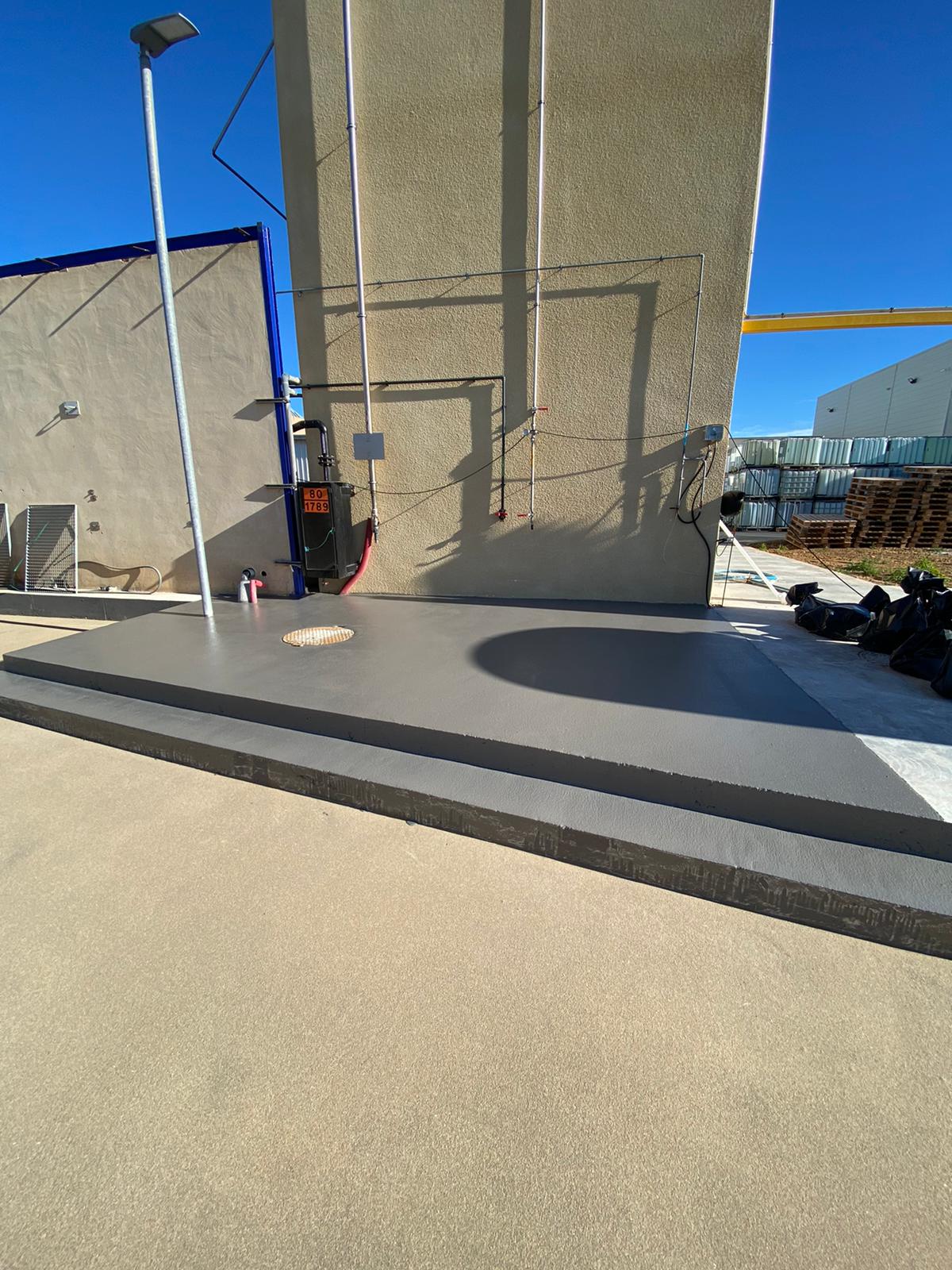 Allée en béton incurvée avec des bordures en gravier, menant à un bâtiment en pierre.