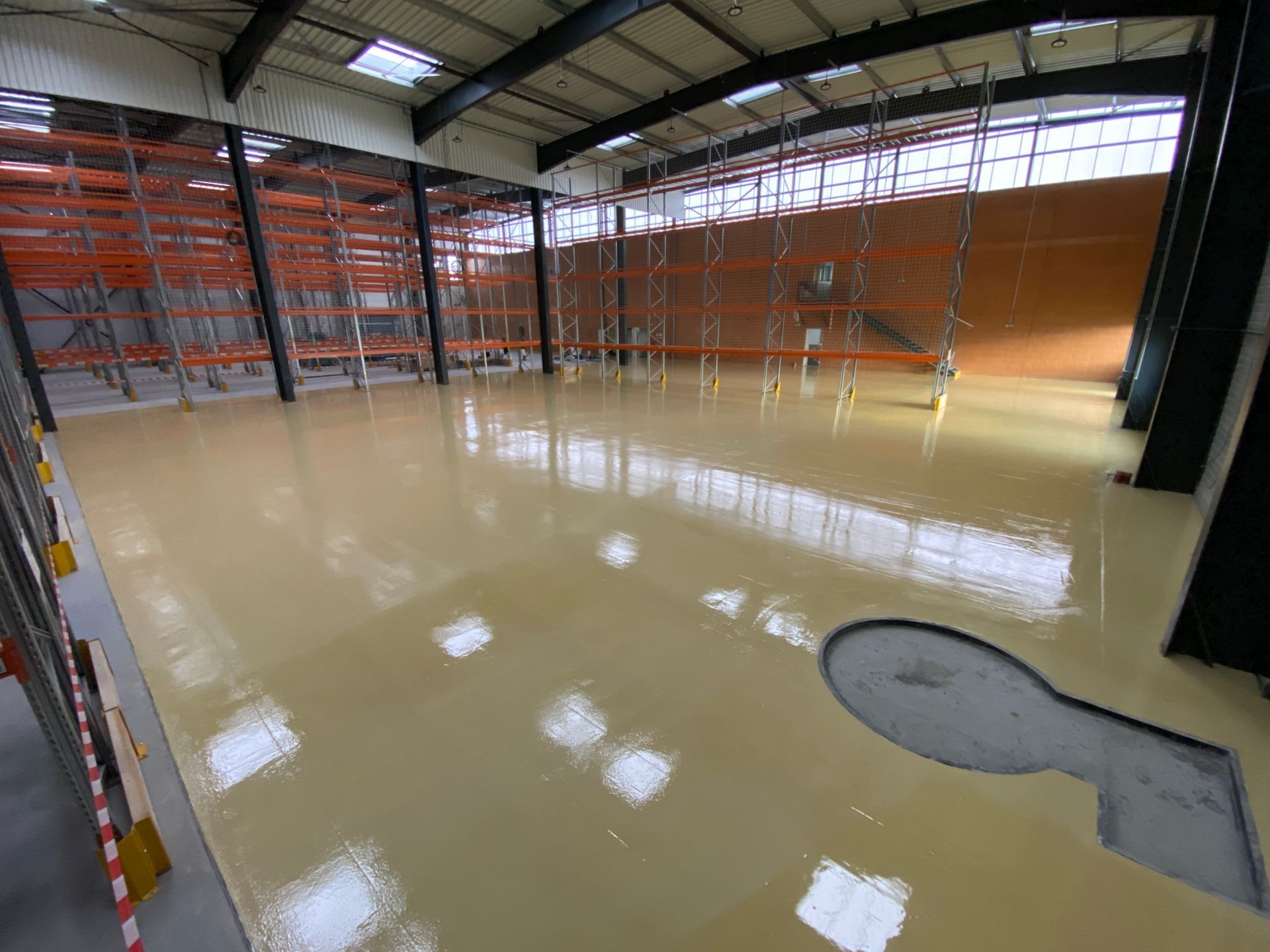 Sol en résine brillante dans un entrepôt, avec des étagères métalliques et des structures en acier.