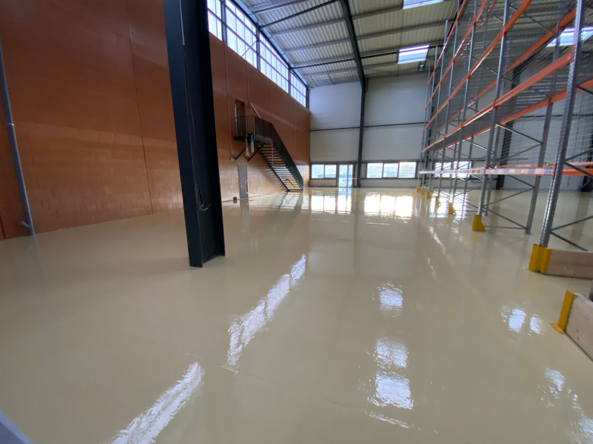 Sol en résine brillante dans un entrepôt, avec des étagères métalliques et des structures en acier.