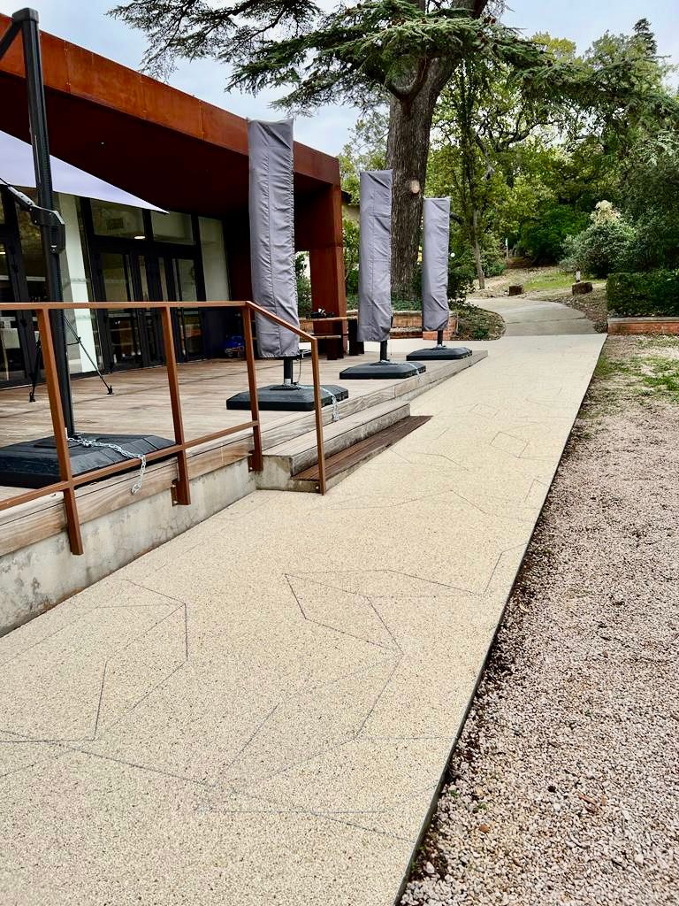 Chemin extérieur en béton avec des barrières métalliques et des bordures en gravier.