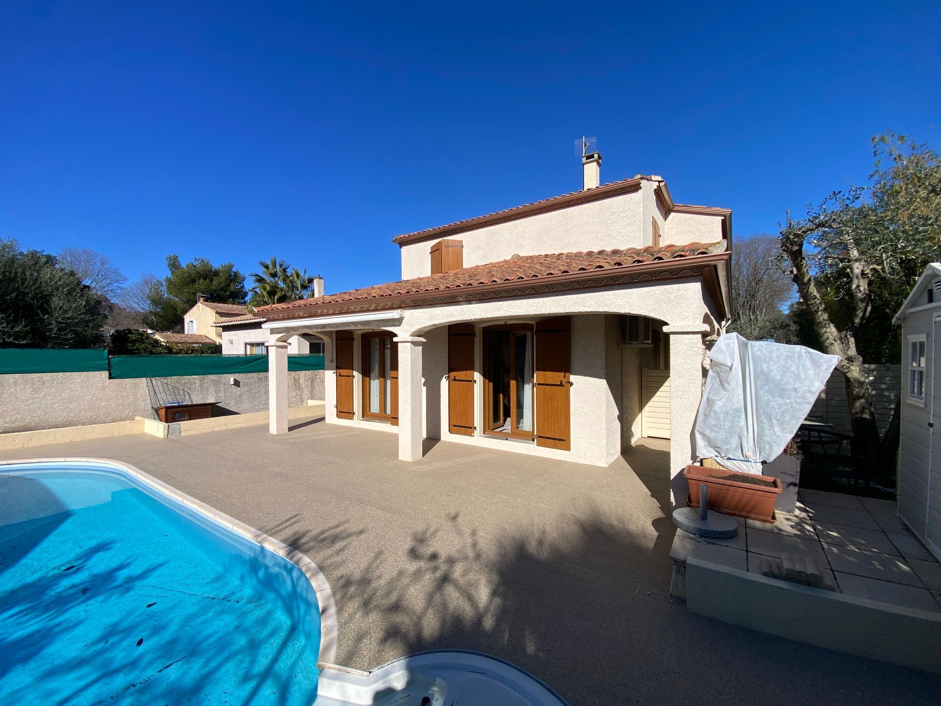 Maison avec piscine et allée en gravier, sous un ciel bleu clair.