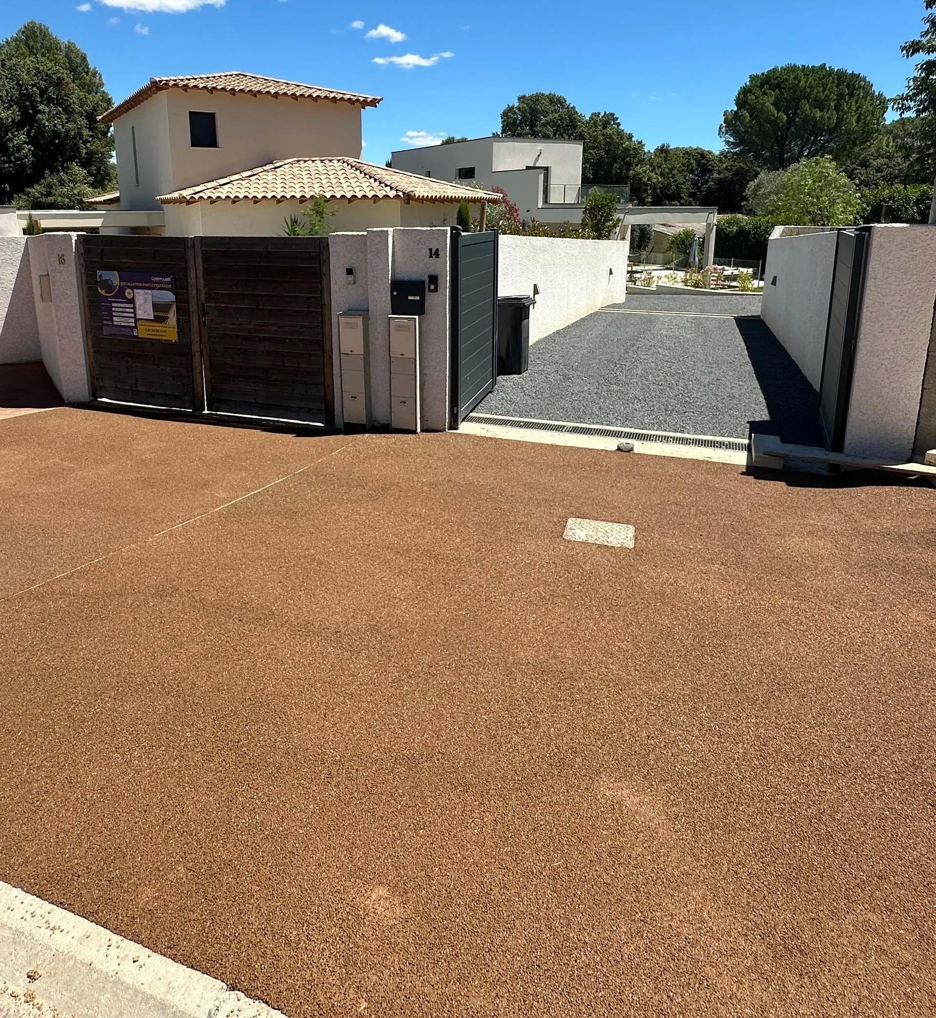 Allée en gravier rouge qui donne sur une allée de gravier gris avec portail ouvert.