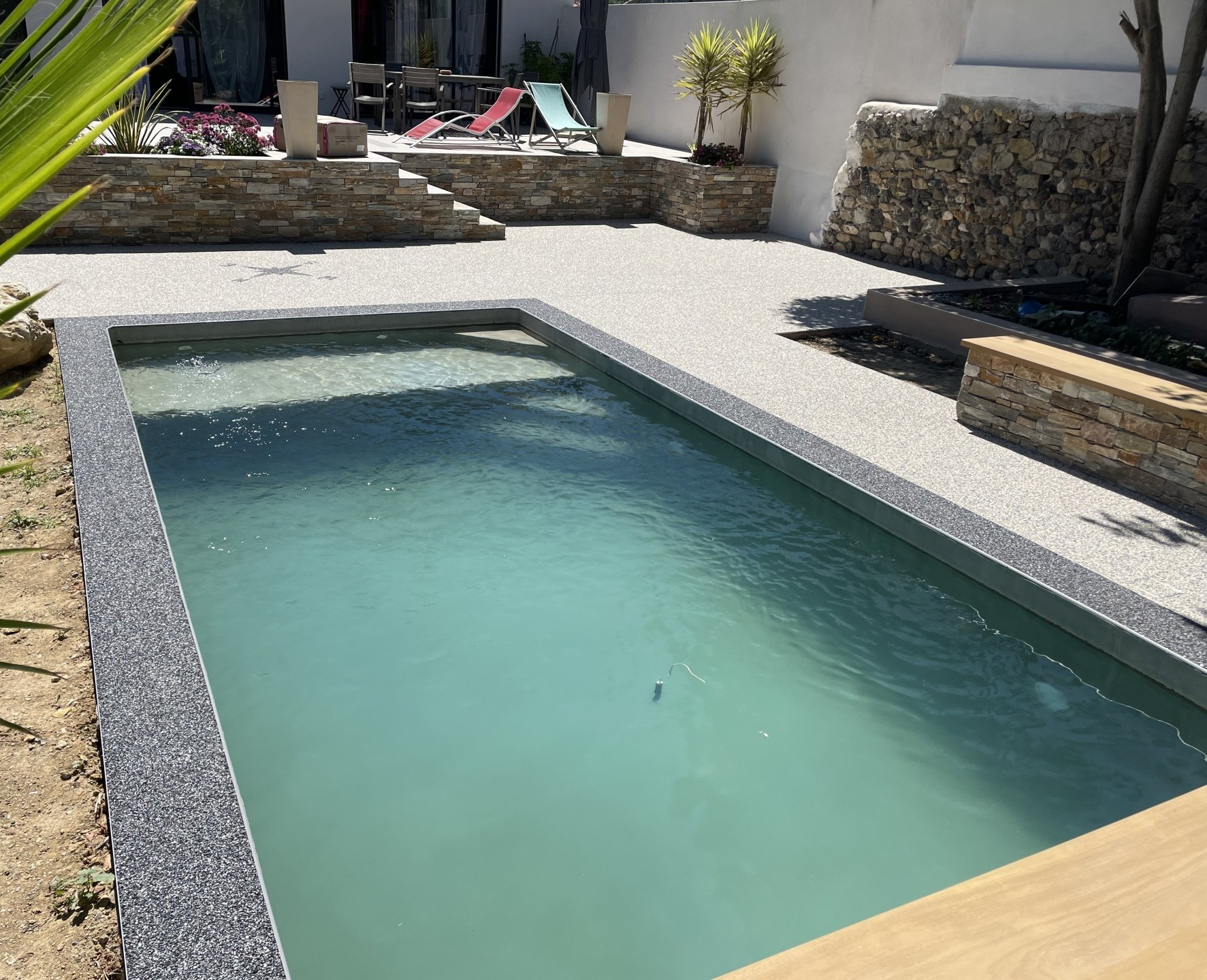 Superbe extérieur de propriété, piscine creusée entourée par résine drainante grise, bois et terre.