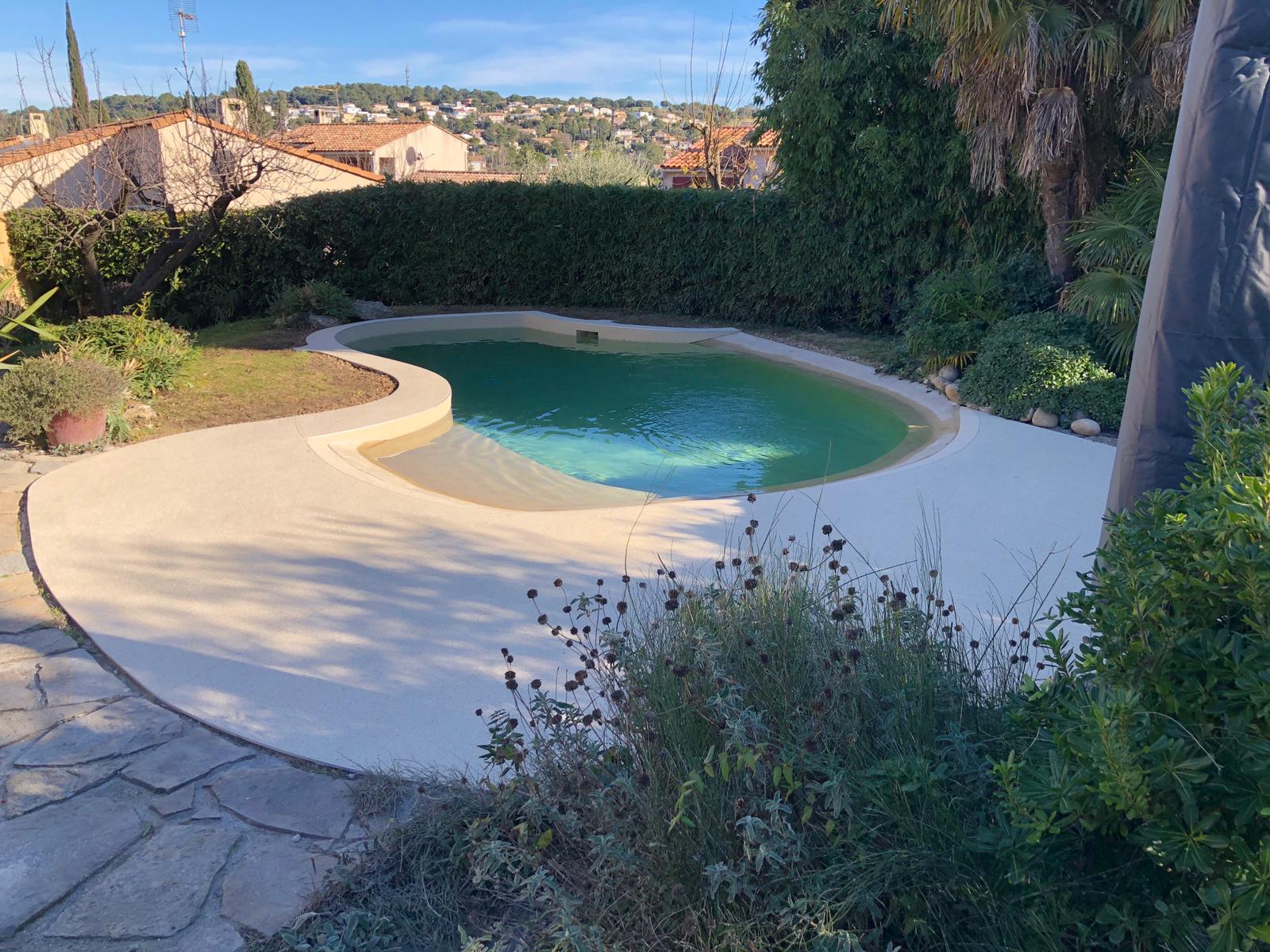 Résine drainante coulée autour d'une petite piscine creusée ombragée, vue sur le village.