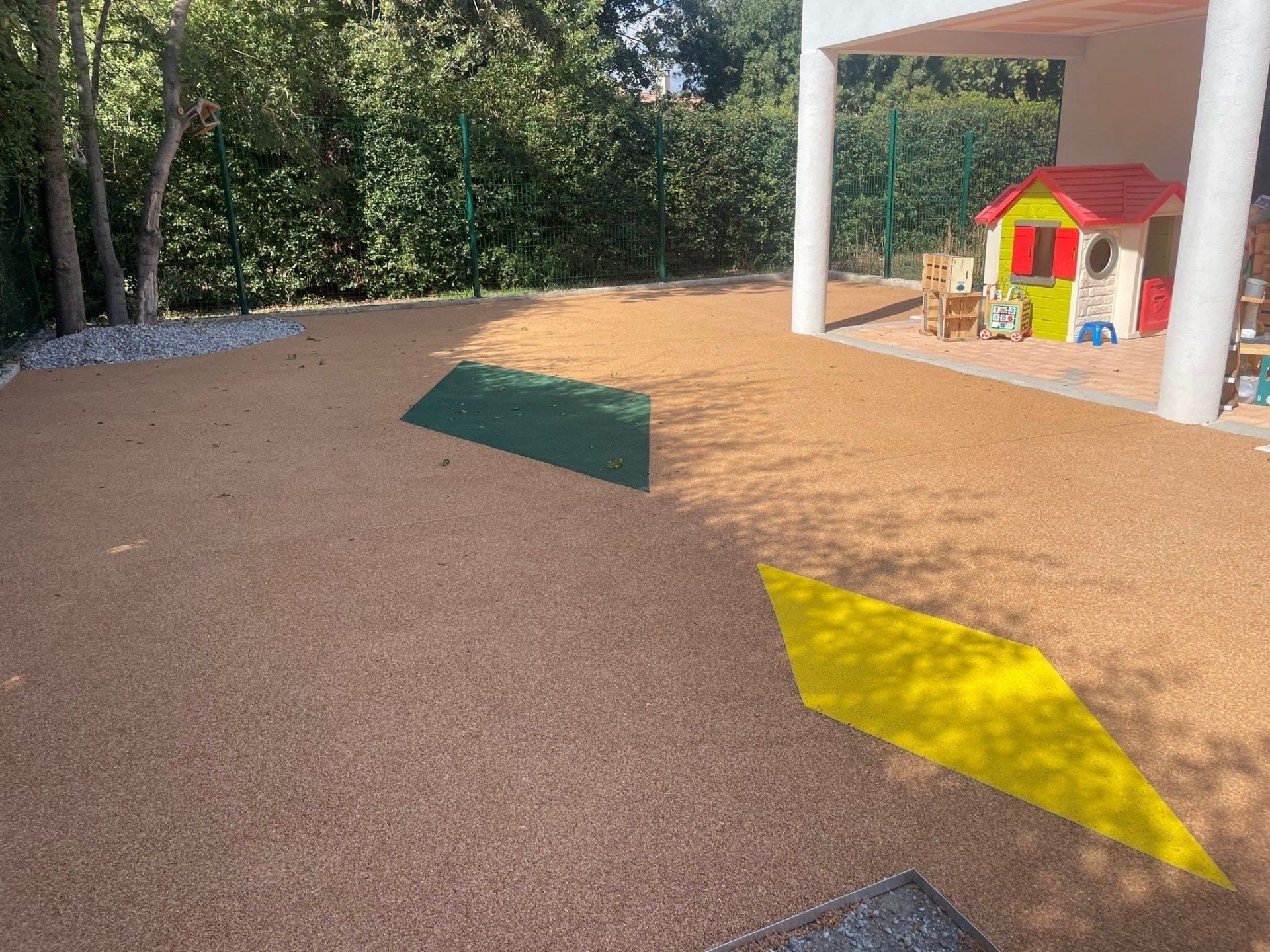 Allée en gravier rouge avec des marques de peinture jaune et verte, menant à une maison.