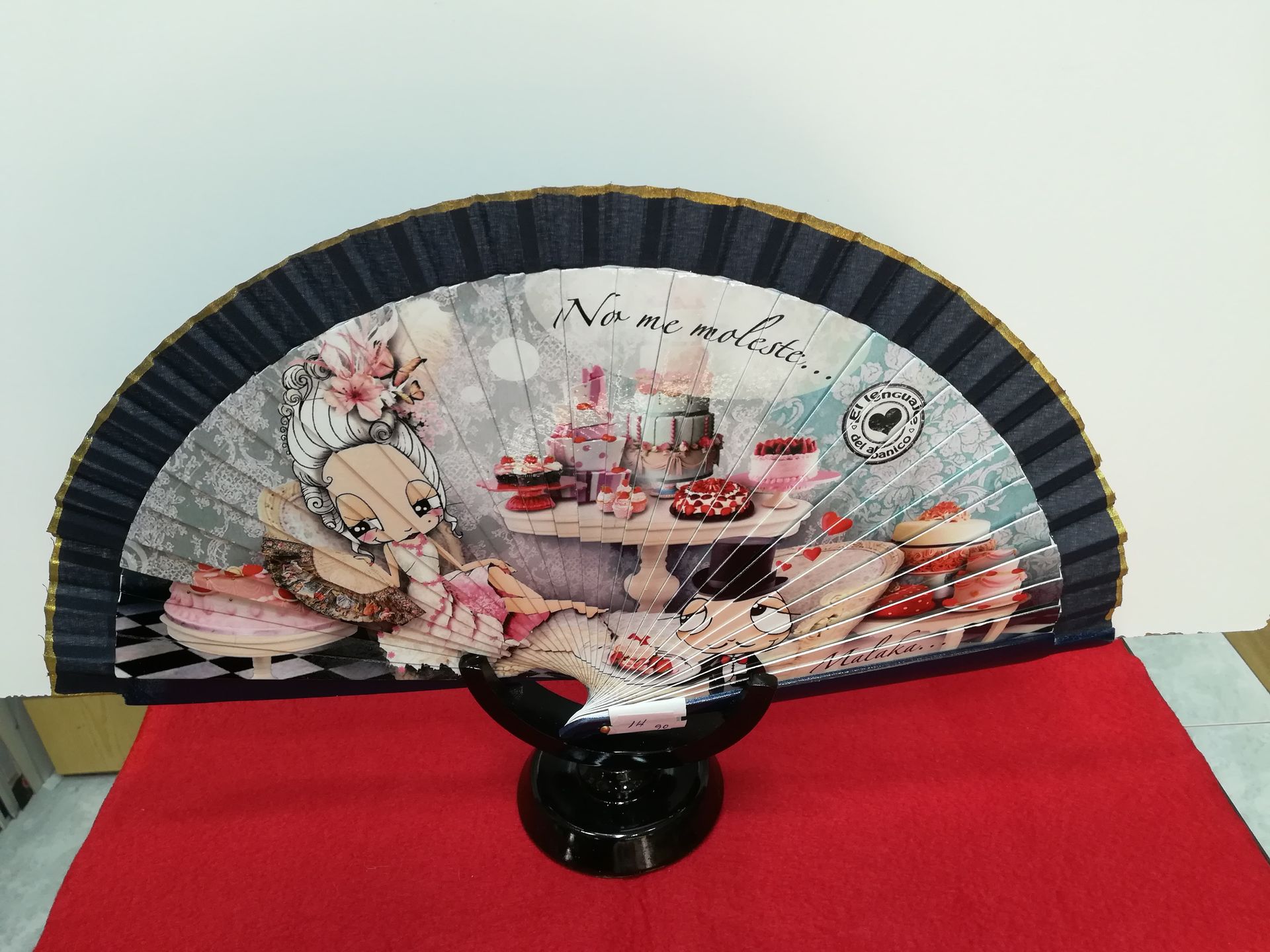 Un abanico con la imagen de una mujer sentada en una mesa y las palabras 